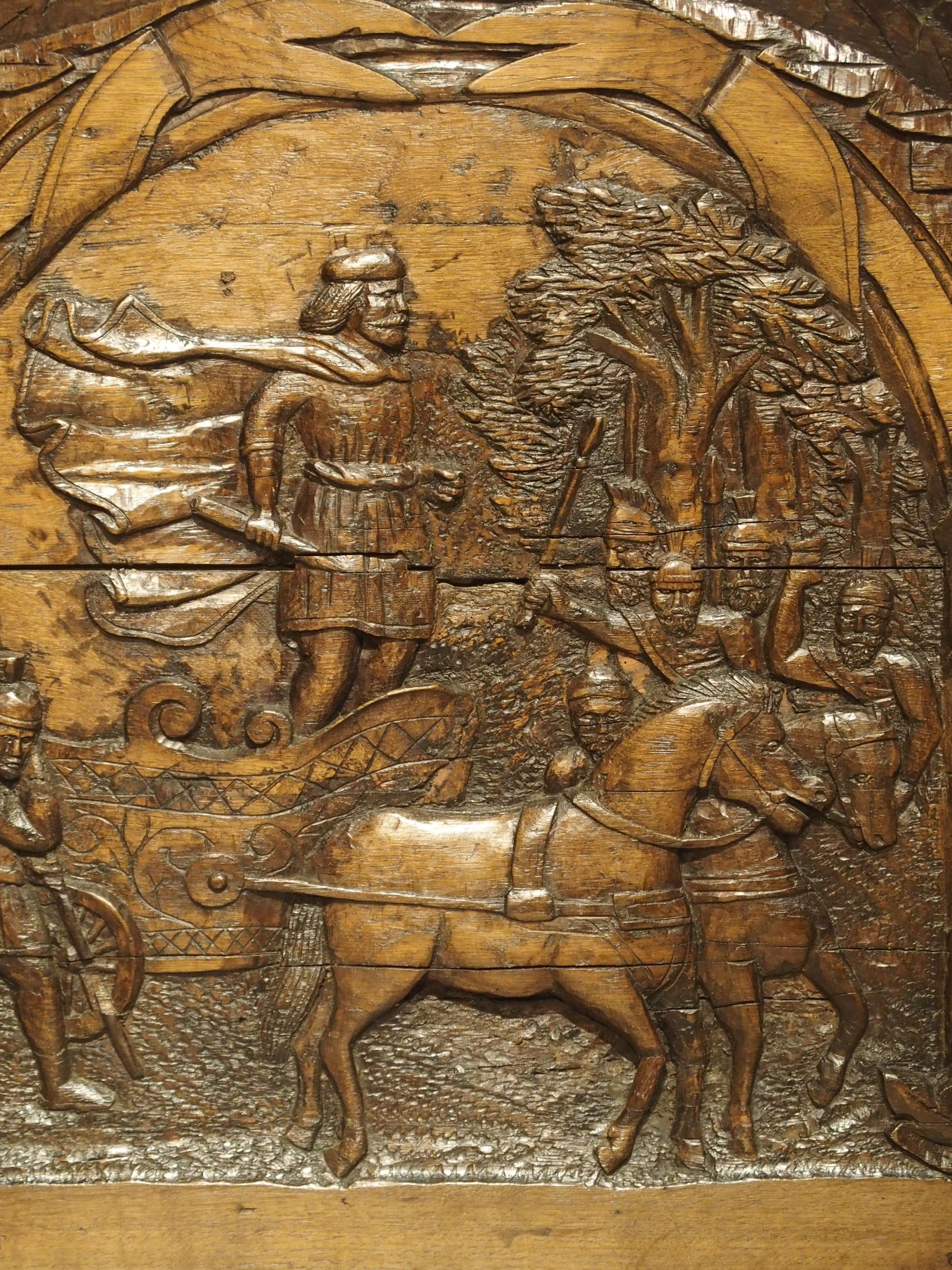 This hand carved antique French panel depicts the arrival of an important figure in a chariot drawn by two horses. Soldiers in front of him coming from a forested background are greeting him. The entire scene is surrounded by stylized beribboned