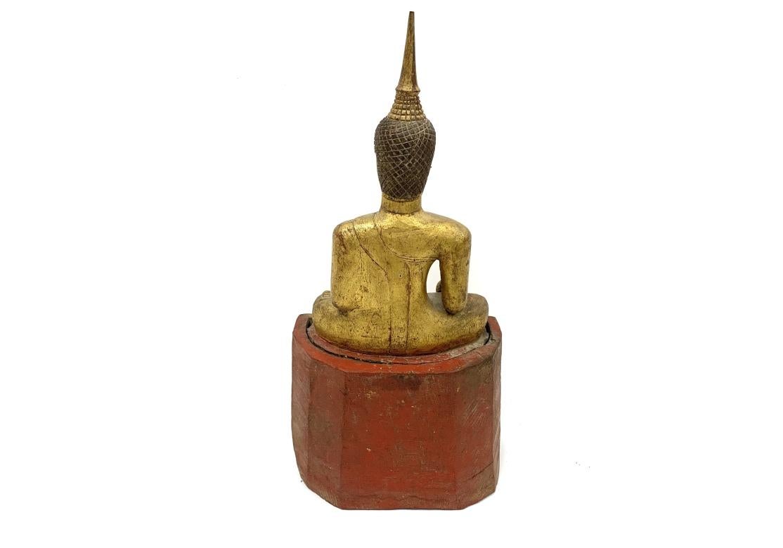 Bouddha de temple très fortement sculpté. Figure de bouddha antique d'Asie du Sud-Est, sculptée et dorée, portant une haute coiffe pointue et assise, une main pointant vers la terre et l'autre main ouverte pour un objet aujourd'hui manquant. La tête