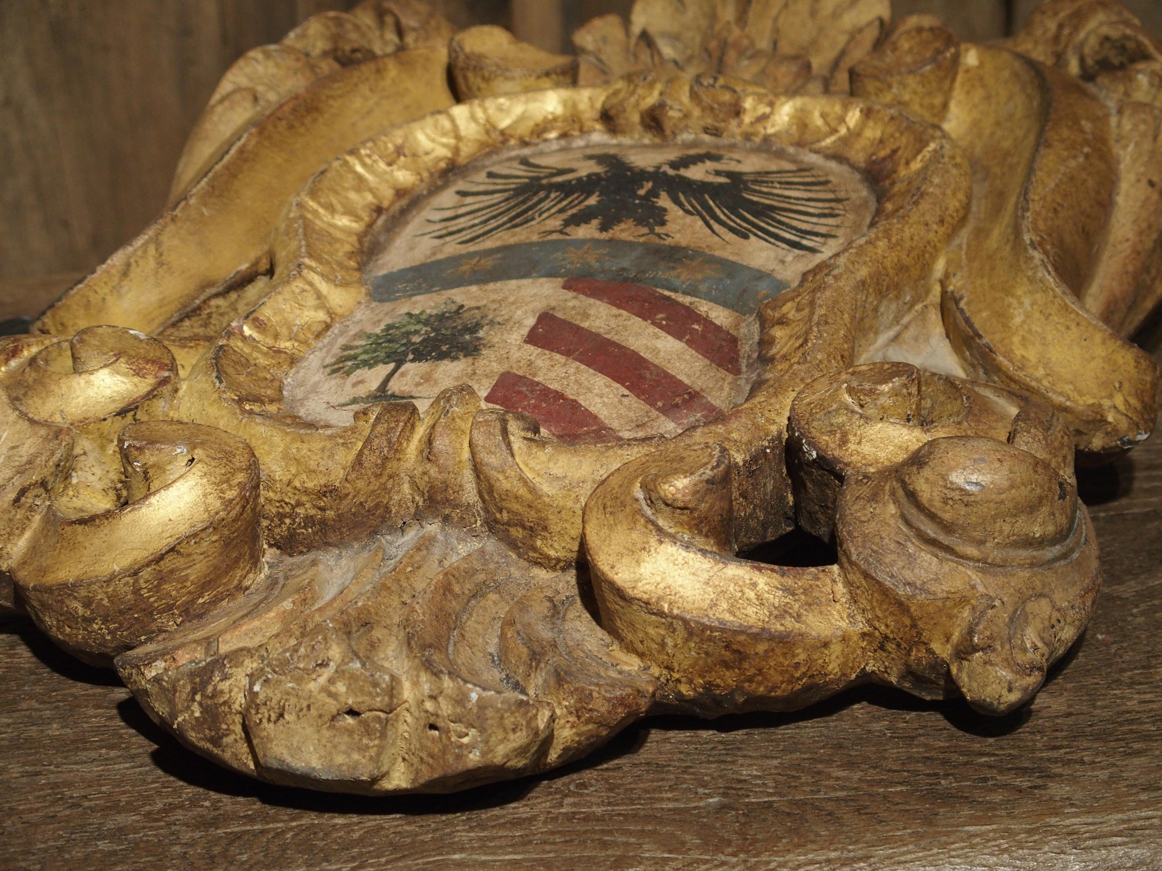 From the 1700’s, this hand carved giltwood and polychrome wooden plaque on stand is from Northern Italy. The subject is an Italian coat of arms surrounded by an acanthus leaf cartouche. There are graceful C-and S-Scrolls in the cartouche that