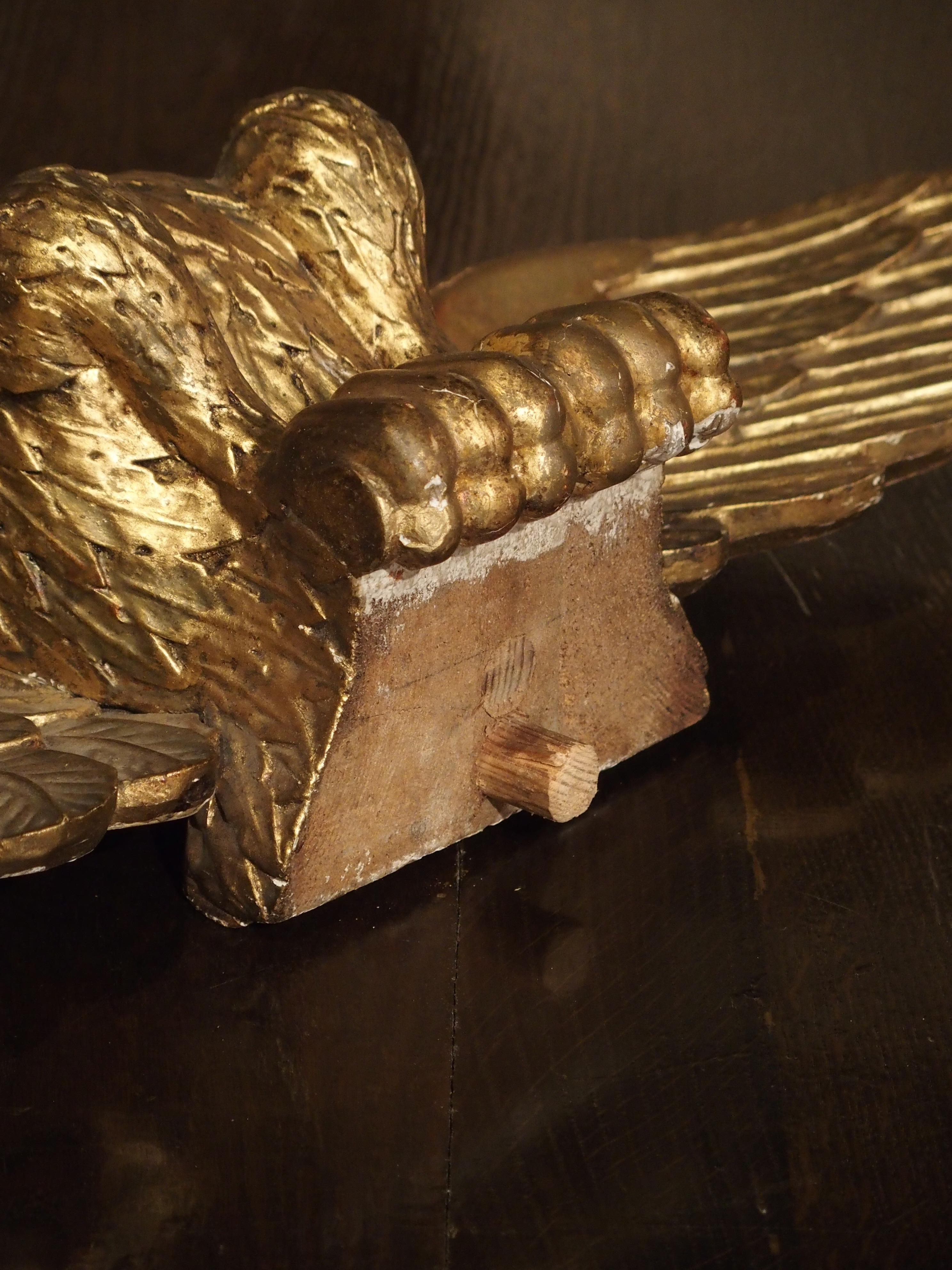Cette statue d'aigle en bois doré sculpté est représentée avec des ailes déployées et des pattes relevées, comme si elle venait de se poser sur quelque chose. Il y a une cheville en bois au bas de la statue, ce qui indique qu'elle était autrefois