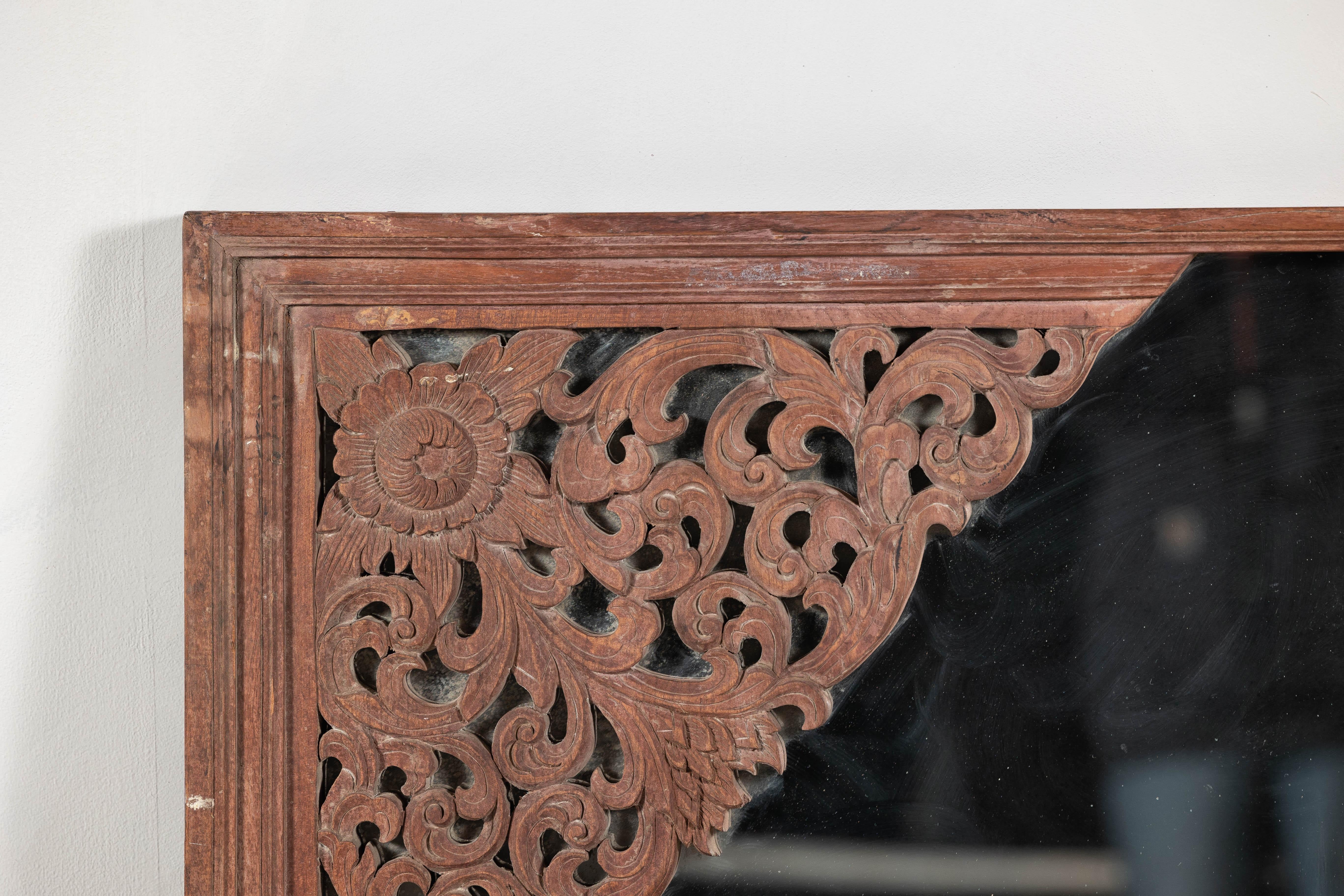 Miroir du début du 20e siècle récupéré d'un élément architectural, cette pièce capture l'essence d'un artisanat complexe et d'un design intemporel. Encadré en bois dur massif patiné par les intempéries, il présente des motifs de volutes profondément