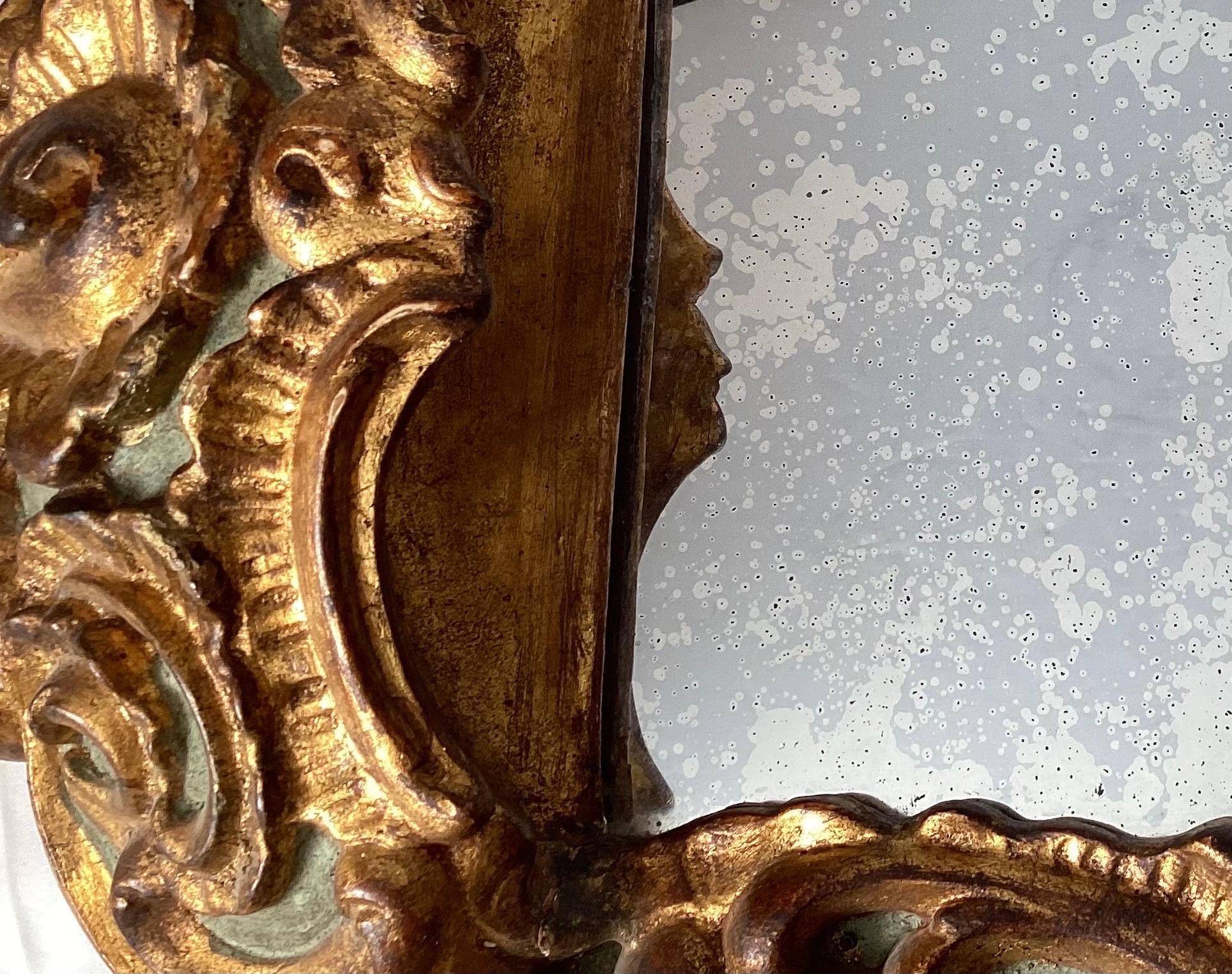 A smaller ornate giltwood mirror with aged looking glass panel. The detailed frame with mirror with an aged silvering reflective surface. The mirror is smaller, 27.5 high, 19 wide. Early 20th Century, Italy.