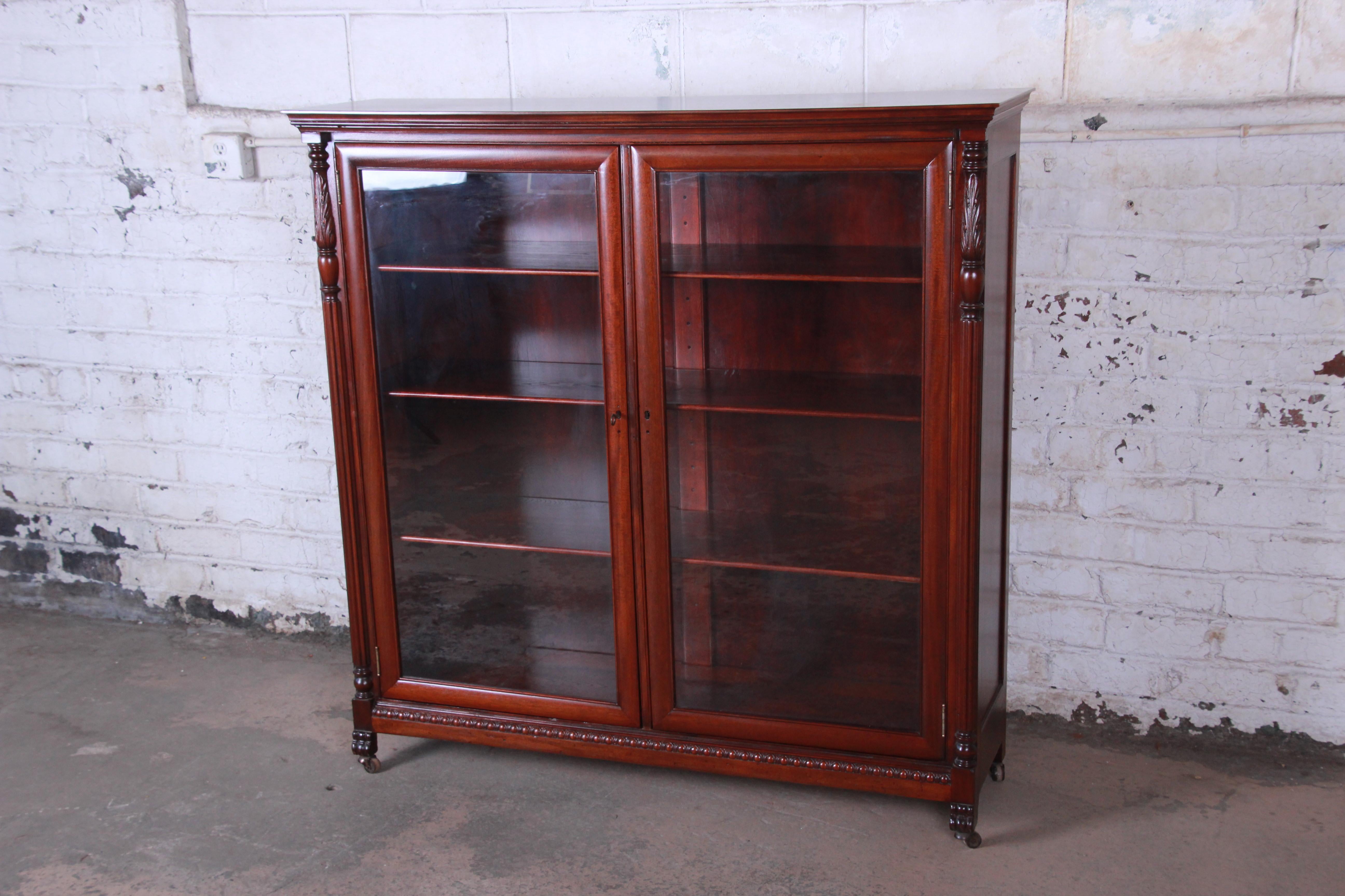 A beautiful antique carved mahogany glass front double bookcase. The bookcase features gorgeous carved details and solid mahogany construction. It offers excellent storage and display, with three adjustable shelves behind two glass doors. The
