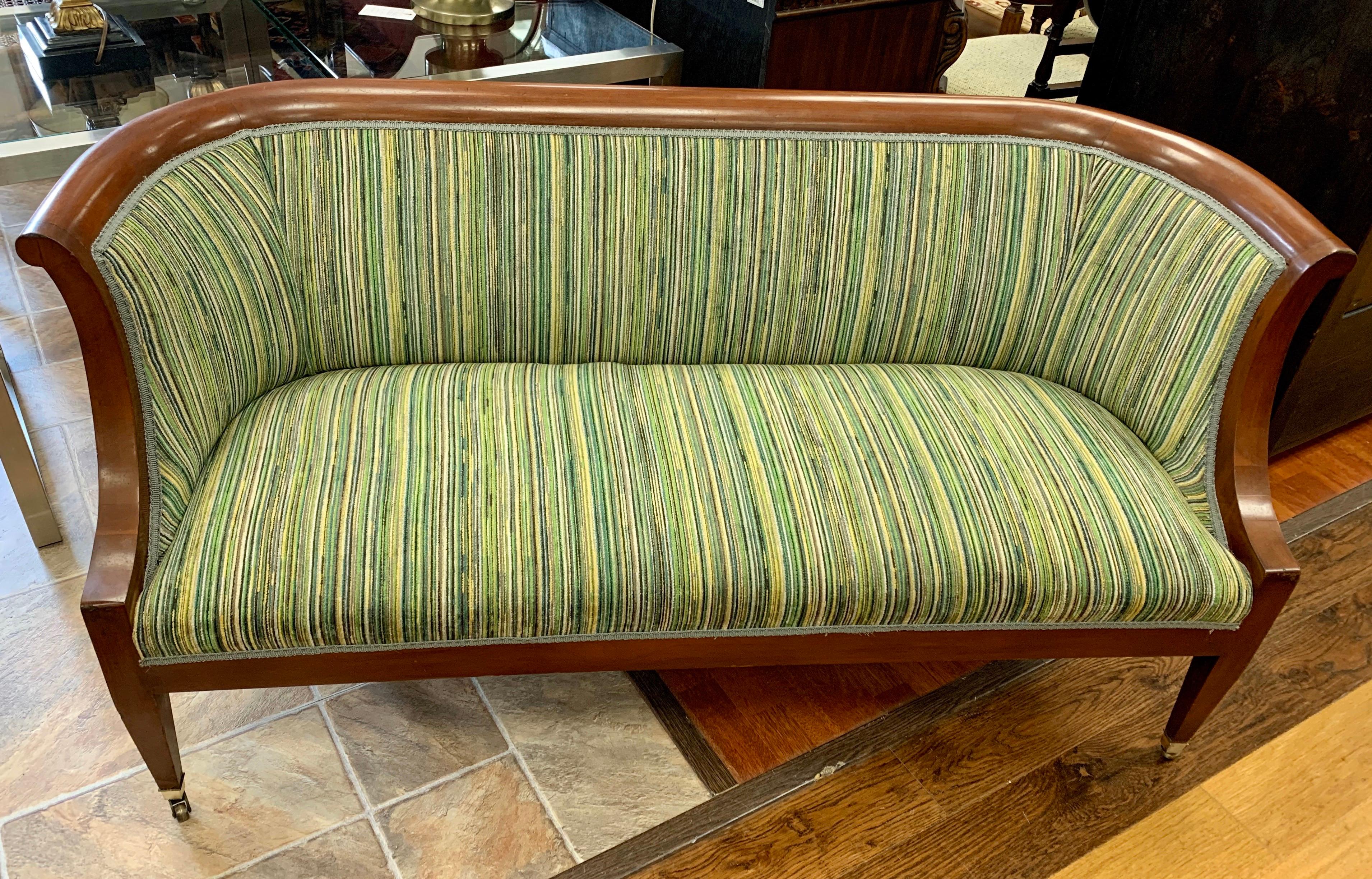 An antique mahogany settee with a straight back that curves gracefully at the arms. Upholstery is brand new and has a textural stripe in green, creams and blue. Front legs have brass castors. Wonderful lines throughout.