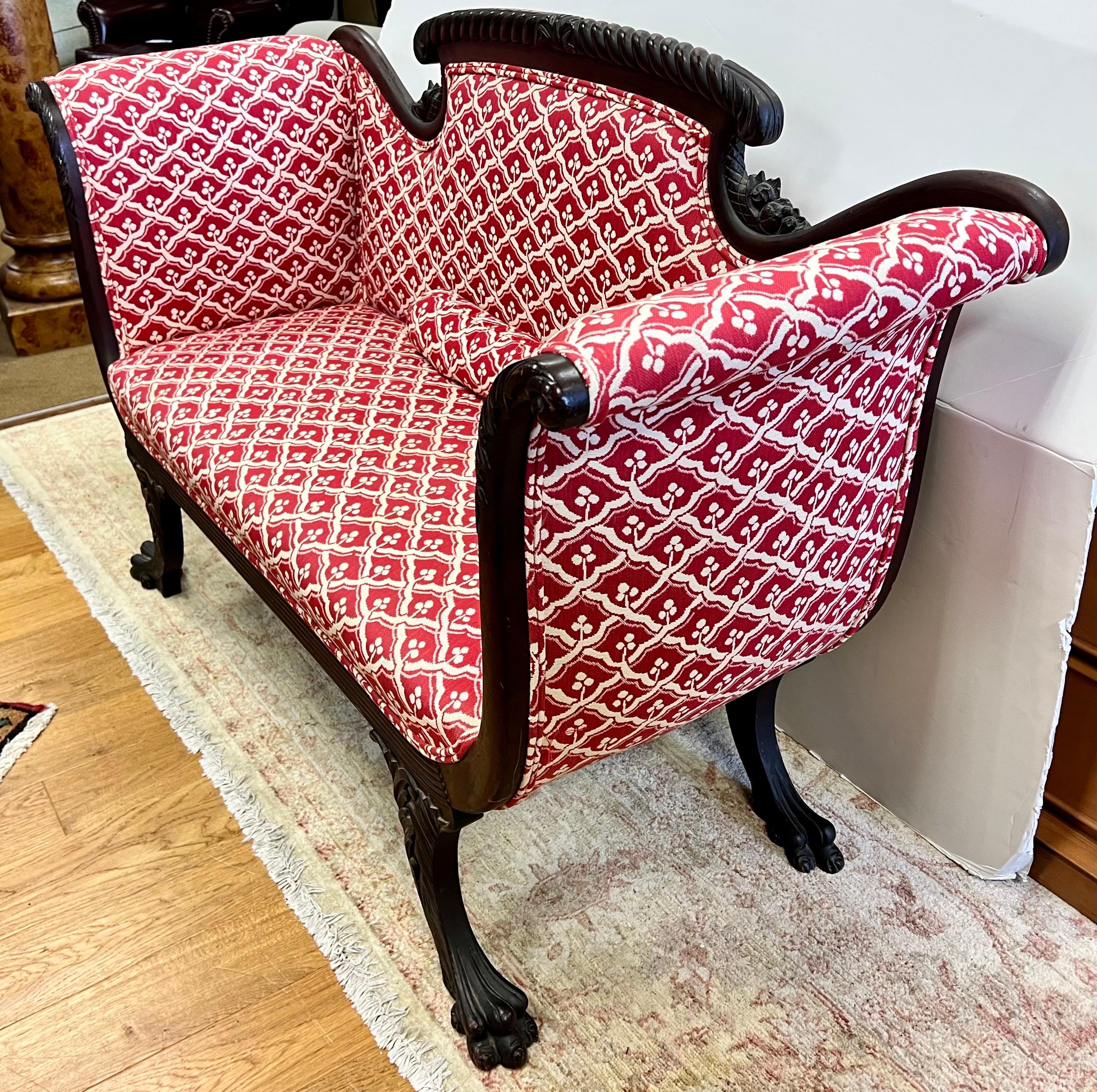 Stunning antique carved mahogany settee features scroll arms and carved claw feet. Newer upholstery is a red and white woven tapestry fabric featuring a petite geometric print of cherries.