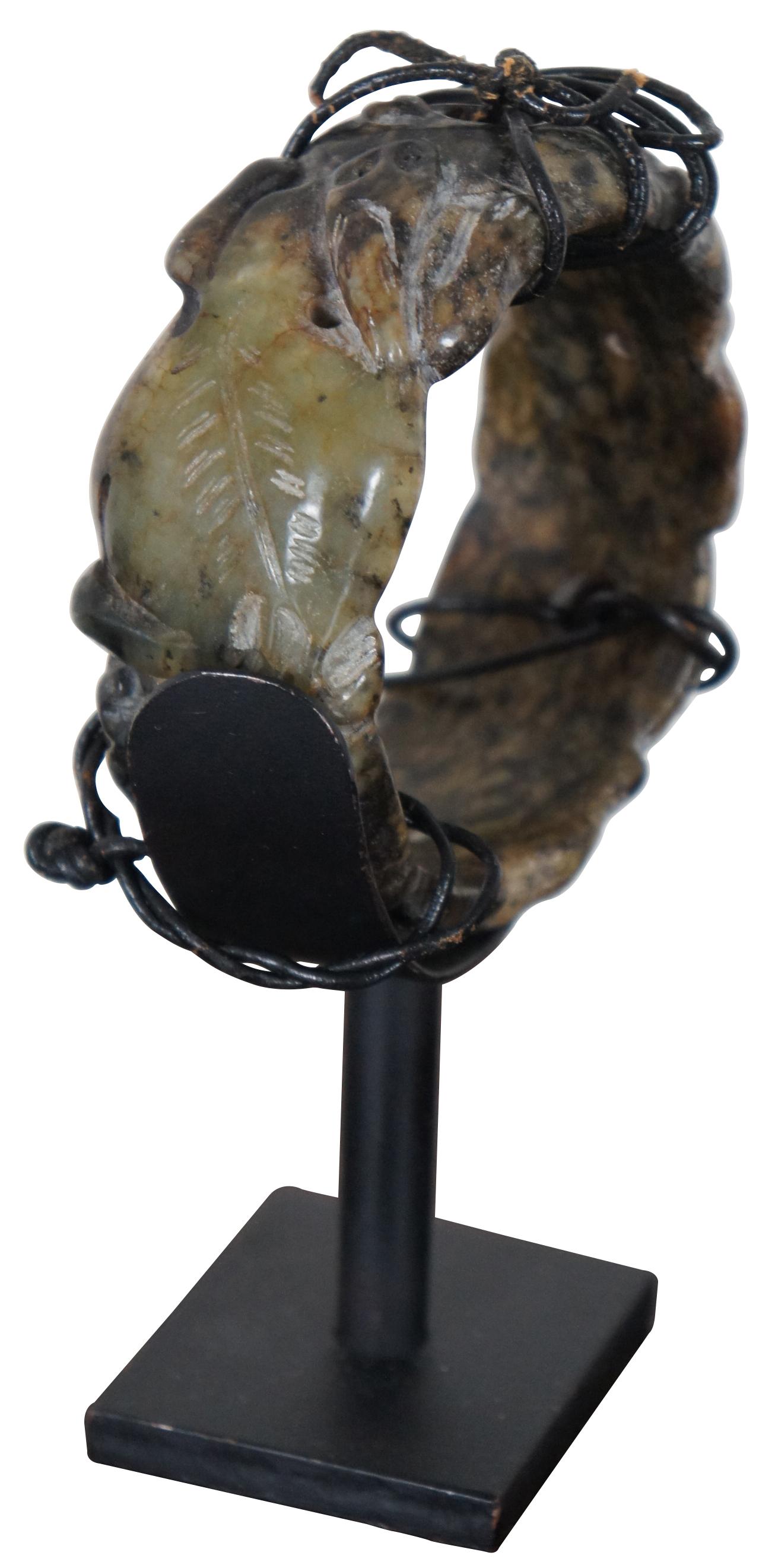 Antique mottled beige and black jadeite bangle bracelet carved with animals and leaves, displayed on a black metal stand.

Measures: 3.5” x 1.75” x 5.5” / Bracelet - 3.25” x 1.25” (Width x Depth x Height/Diameter x Height).