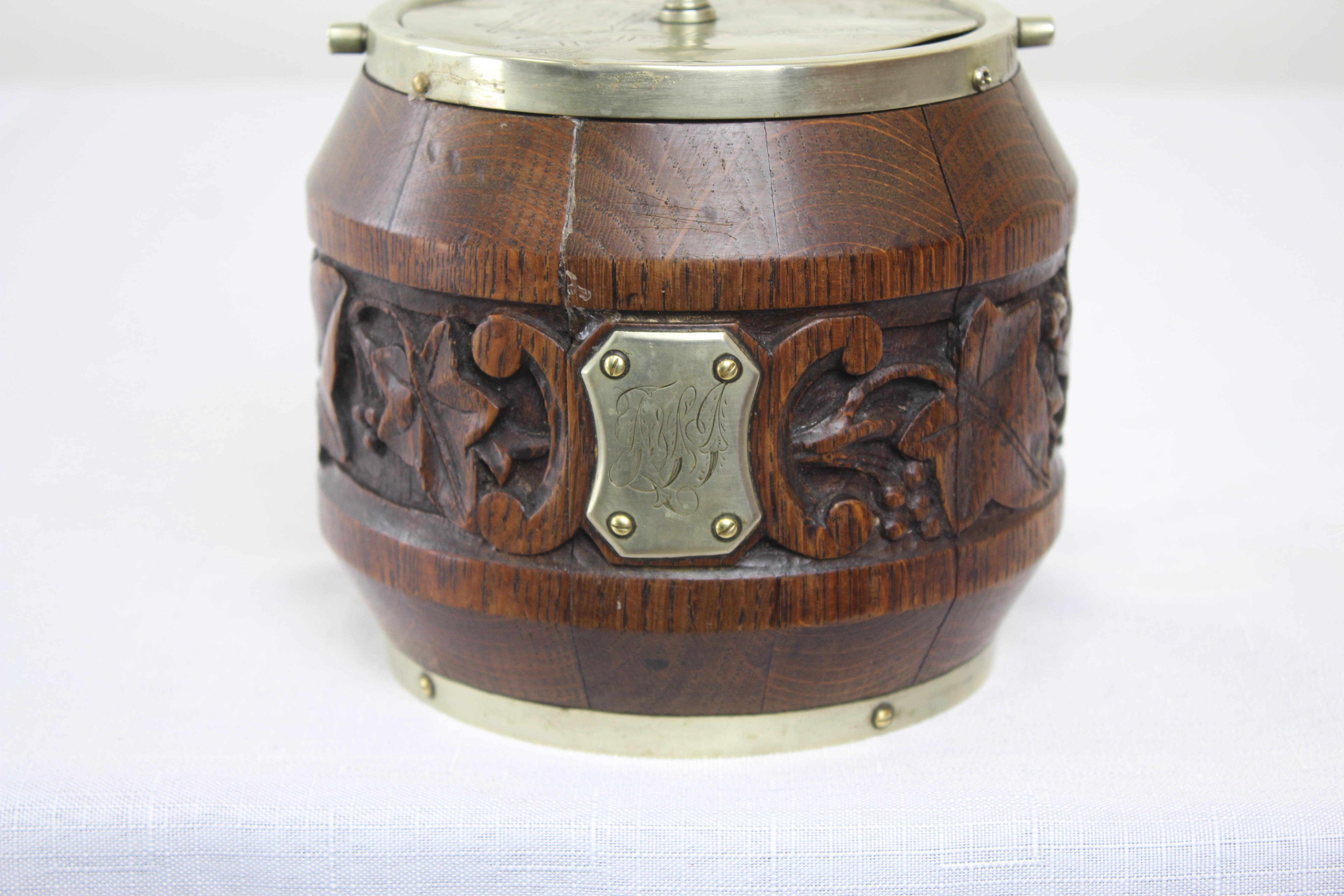 A charming oak biscuit barrel from the late 19th century with a carved grape and leaf pattern. The original owner's initials are etched in the center medallion. The metal is stamped 