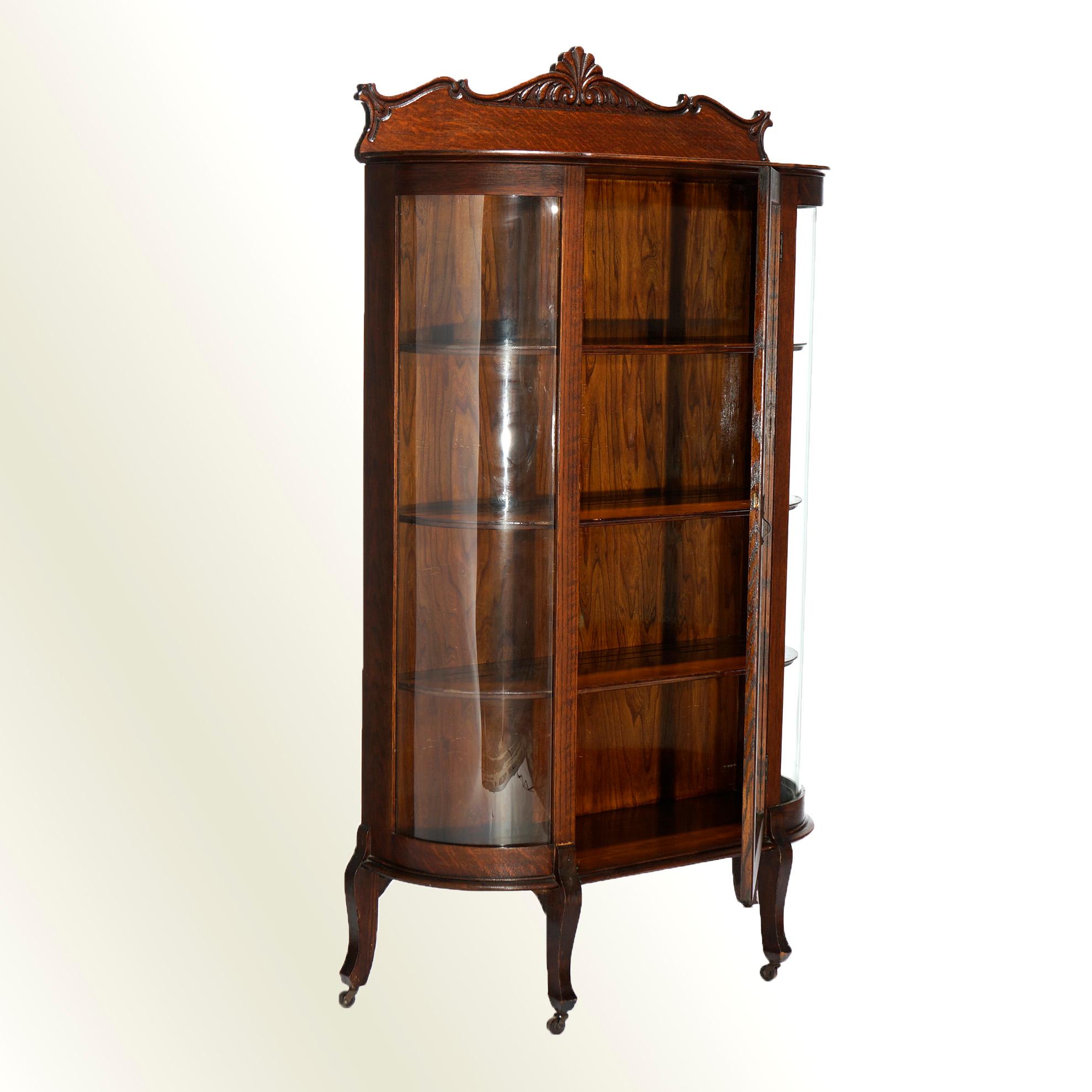 An antique china cabinet offers quarter sawn oak construction with foliate carved backsplash over sing door case having curved glass and opening to shelved interior, raised on cabriole legs, c1900.

Measures- 64.25''H x 37.25''W x