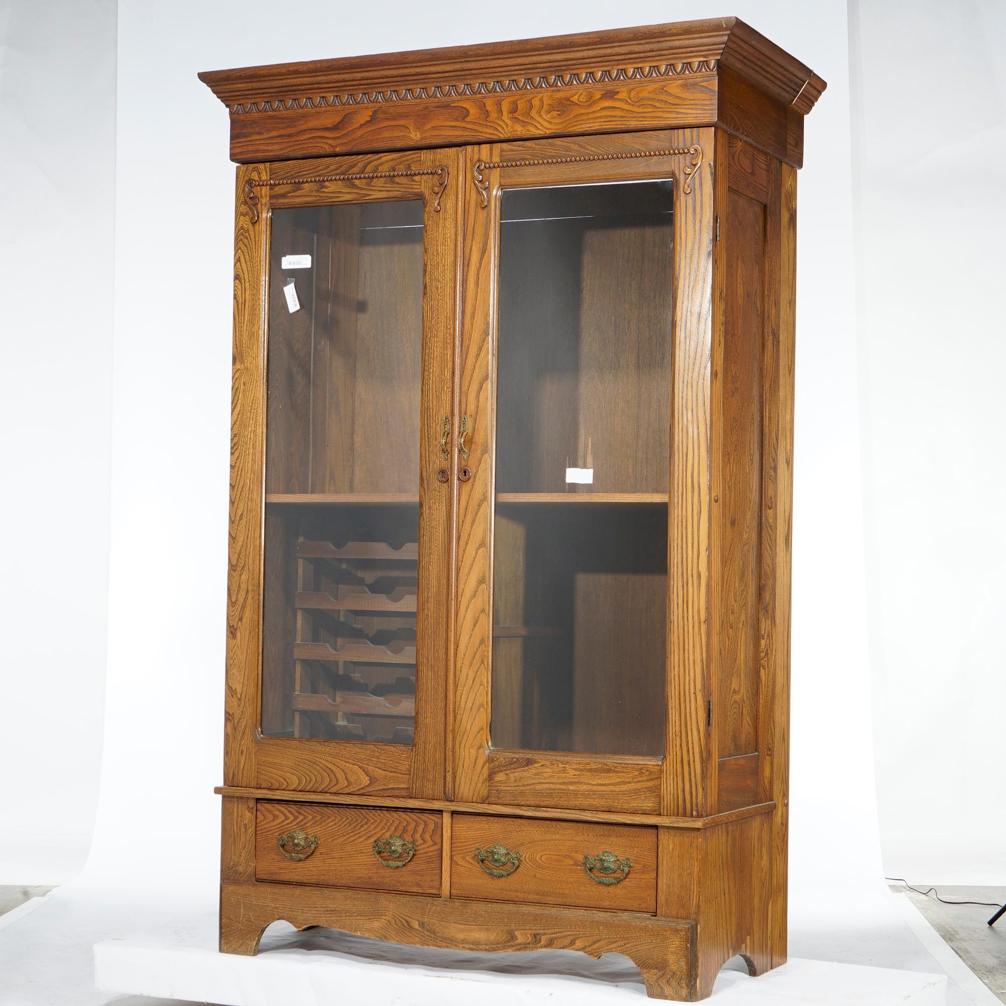 An antique Arts and Crafts bookcase (modified into an entertainment center) offers quarter sawn oak construction with double glass doors opening to shelved interior with lower wine rack over two drawers and raised on bracket feet, later added cord