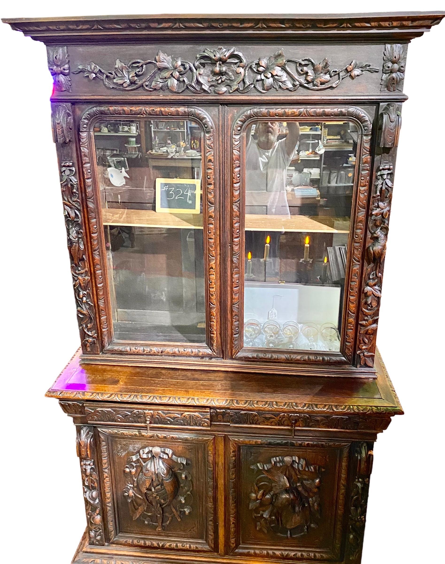 A handsome antique carved oak French Henri II cabinet/cupboard having extensive carving of leaves, tendrils, fish and fruit, glass doors, two carved drawers and two carved wooden doors, with one shelf behind. 

Could be a walk up bar/liquor