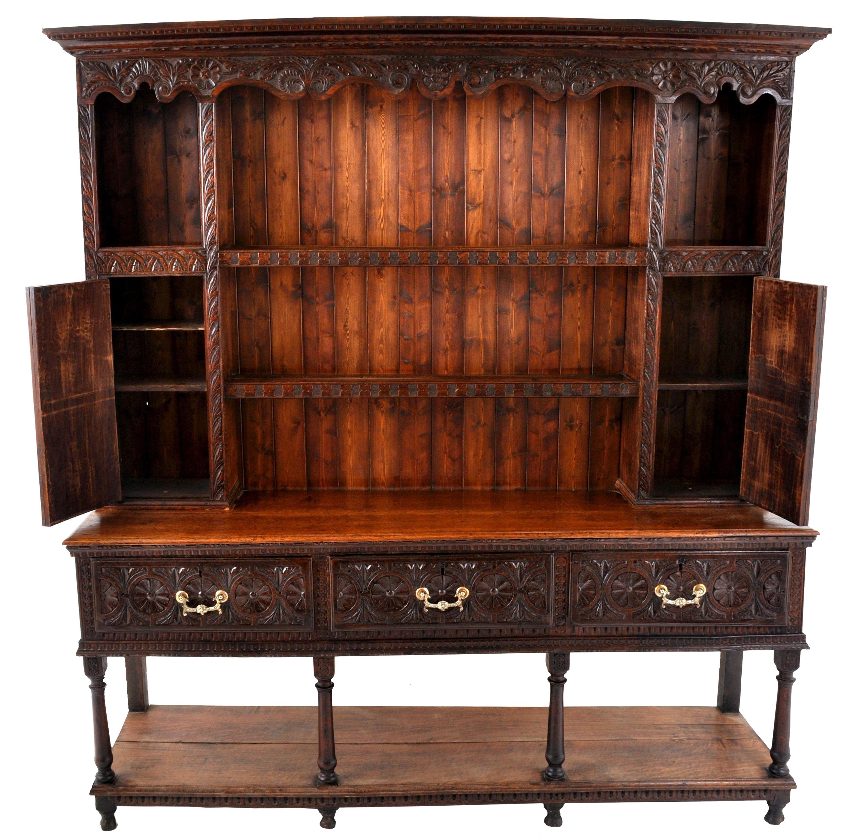 A fine antique Georgian carved oak Welsh dresser/cupboard, circa 1820. To the back is a pot rack with a carved cornice, with a shaped gallery below. The back having carved storage recesses and shelving and two carved cupboard doors with arched