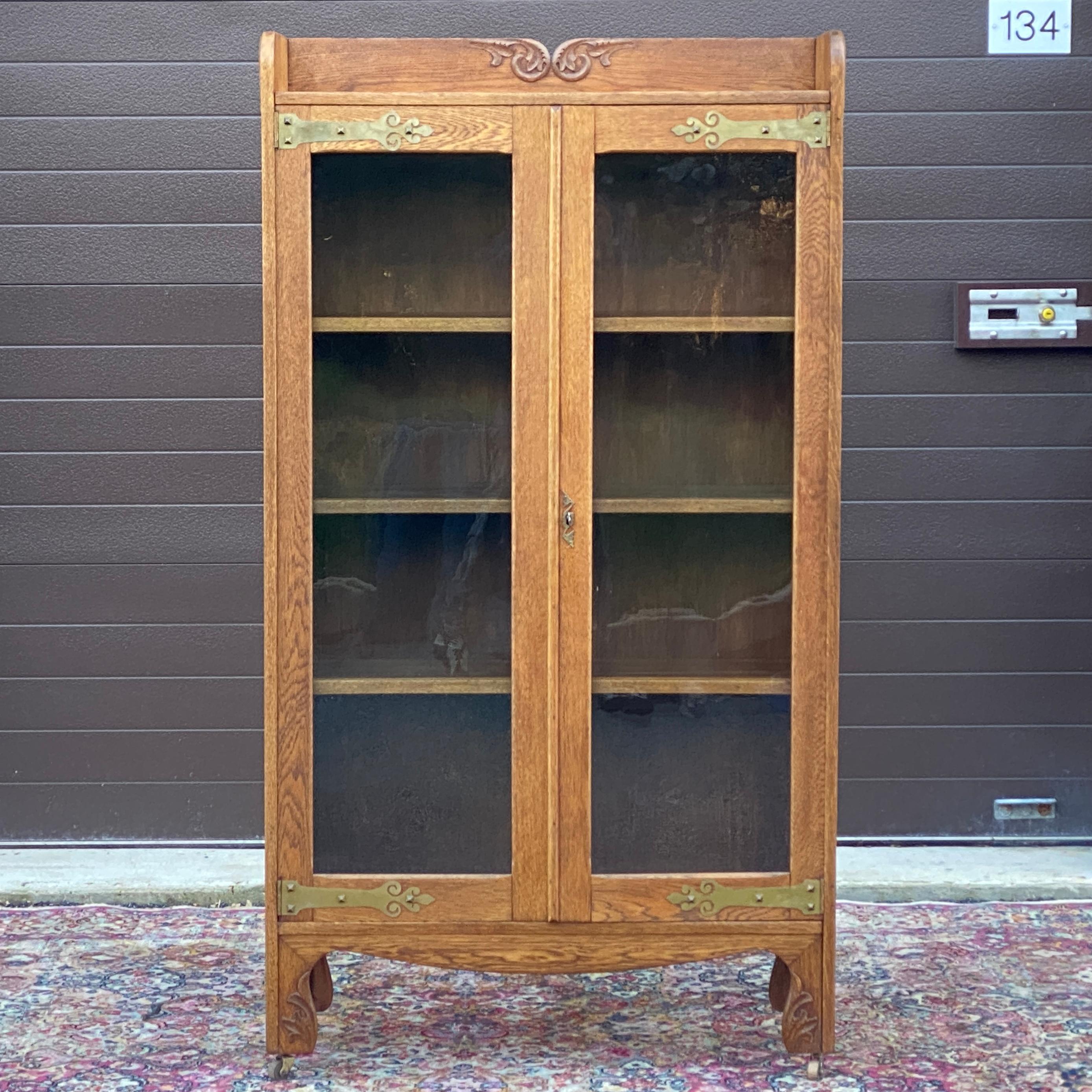 Antique oak locking glass door bookcase with decorative brass hinges and hand carved details. 
Interior adjustable shelves 31.5”w x 9.75”d