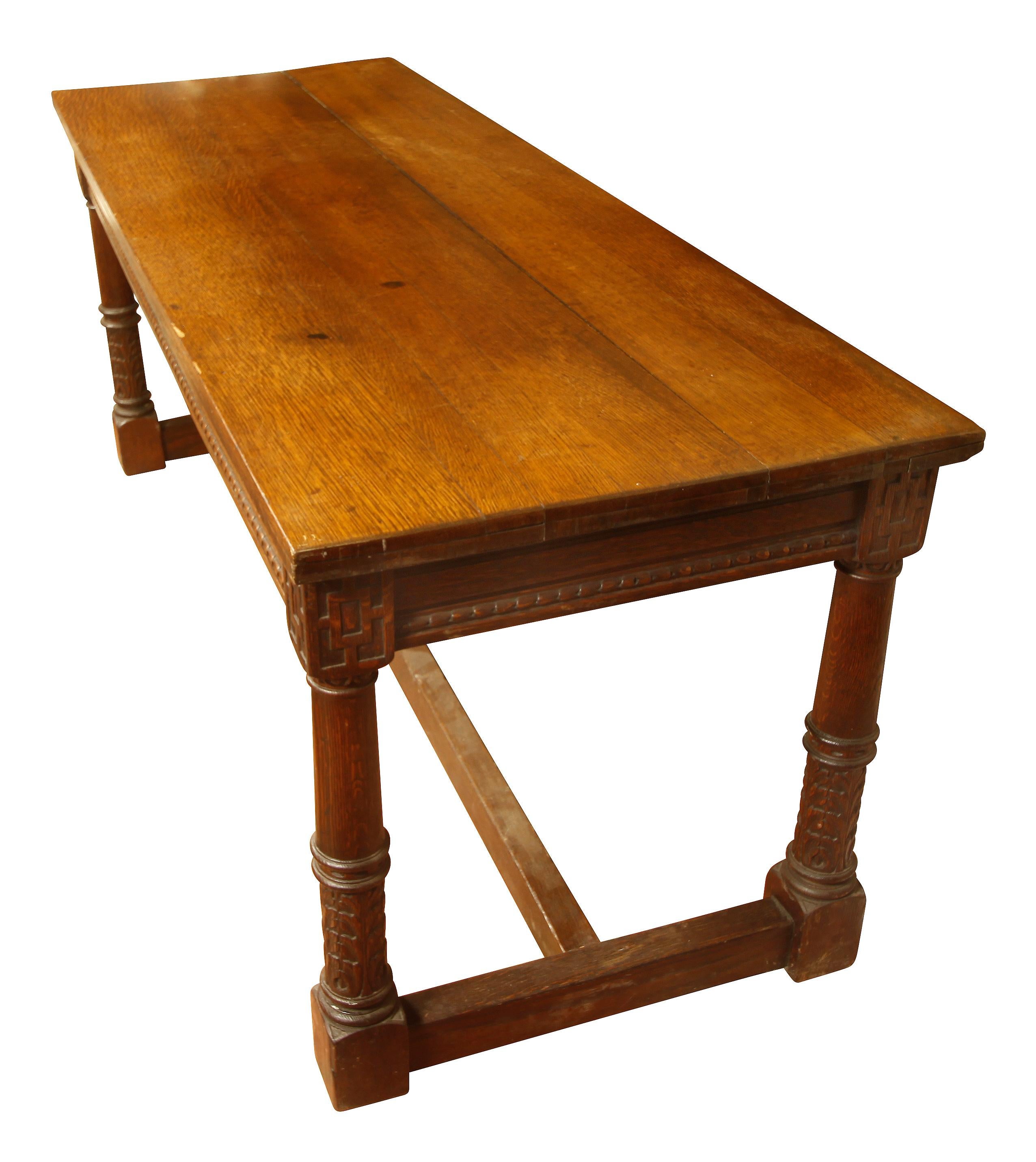 Antique carved oak library table with acanthus leaf detail on the legs, geometric motif at corners, and H-form stretcher at base.