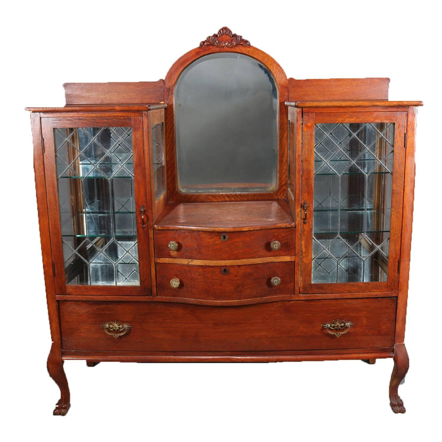Antique China buffet features oak construction with central arched beveled mirror with carved foliate crest above two central drawers and having flanking enclosed glass china displays having glass sides and leaded glass doors opening to
