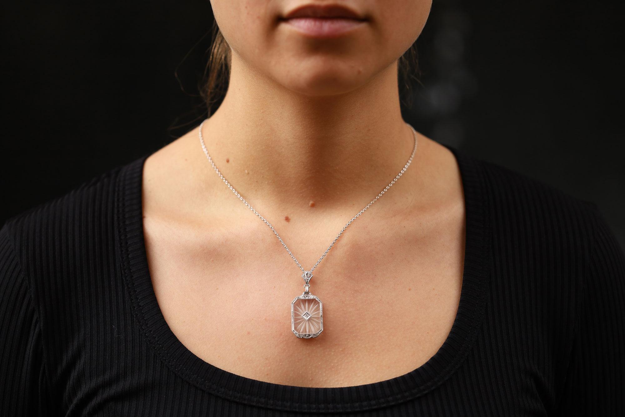 This 1920s antique necklace features beautifully hand carved rock crystal, ever unique and fashionable. With exceptional craftsmanship and intricate, scrolling engraved volute designs, this platinum pendant focuses on a sparkling natural diamond in