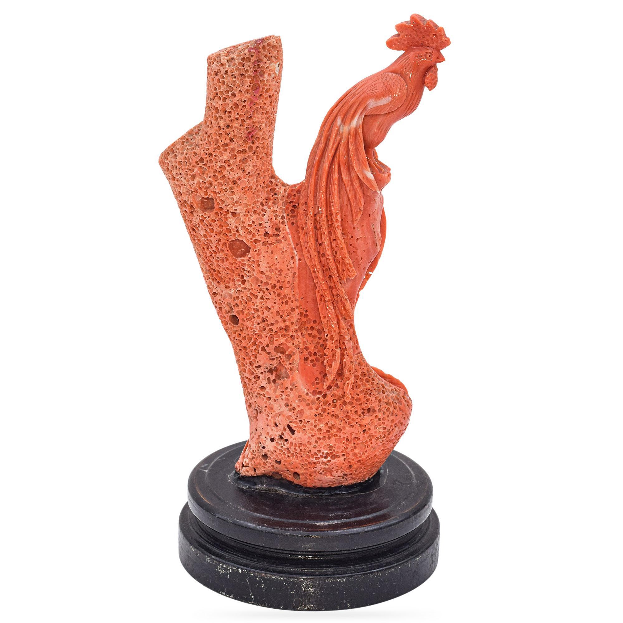 Cette sculpture saisissante captive par son design complexe et sa teinte rouge vibrante. Sculpté dans un seul morceau de corail, il représente un coq perché élégamment à côté d'une branche texturée, ornée de délicats motifs de feuilles, témoignant