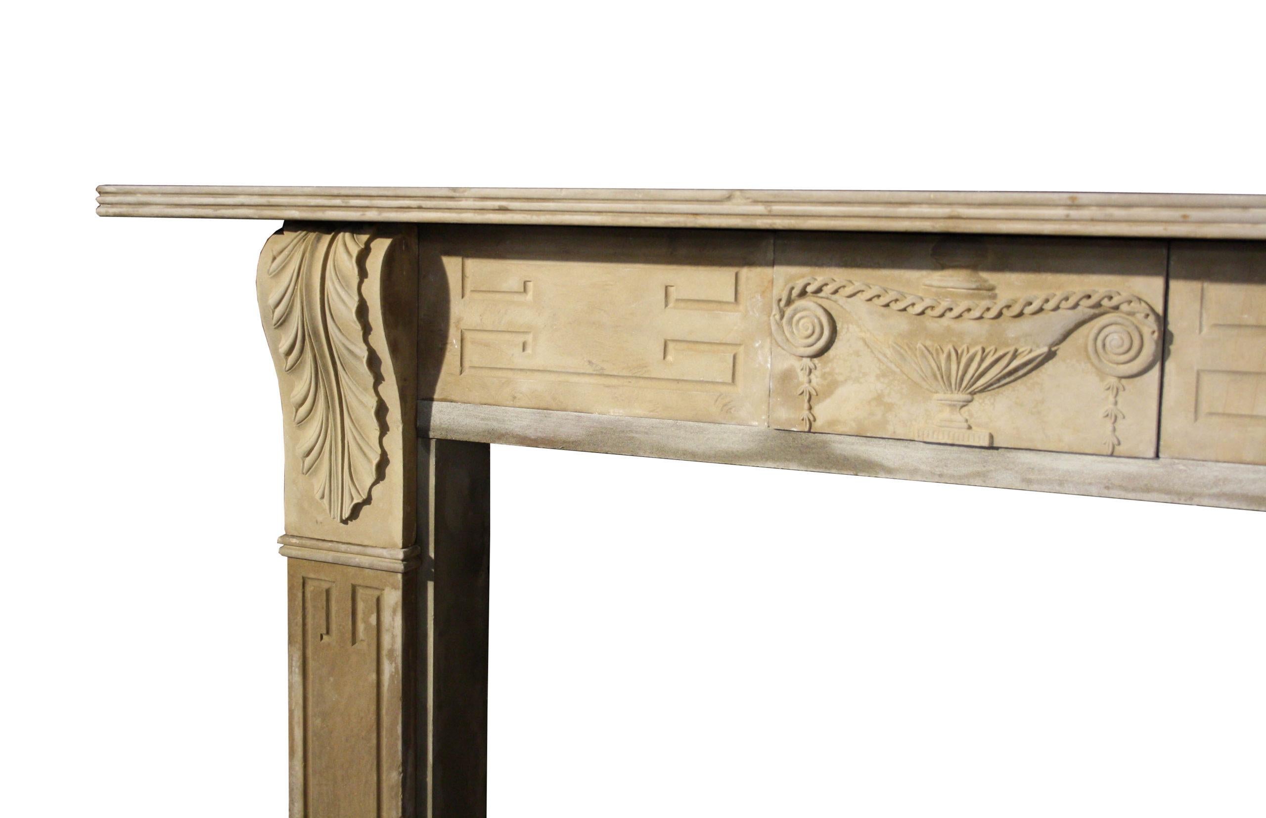A well proportioned English Regency stone fire surround. The jambs with Greek key panels surmounted by carved brackets of classical form. The frieze carved with carved classical urn to centre above a reeded shelf. First quarter of the 19th
