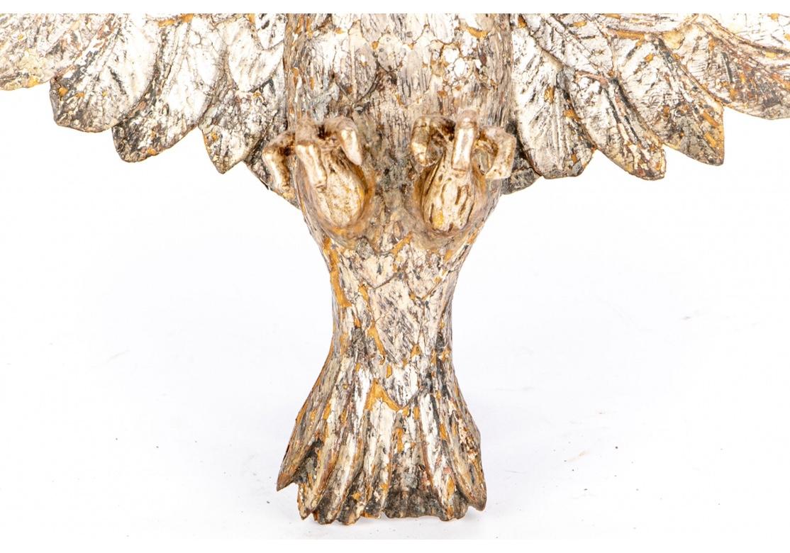 Strongly carved antique wood eagle, probably European, with out spread wings in a Heraldic posture, all in a silver and silver gilt finish. Condition is quite good overall with expected and acceptable loss to the finish and some slight chips, the