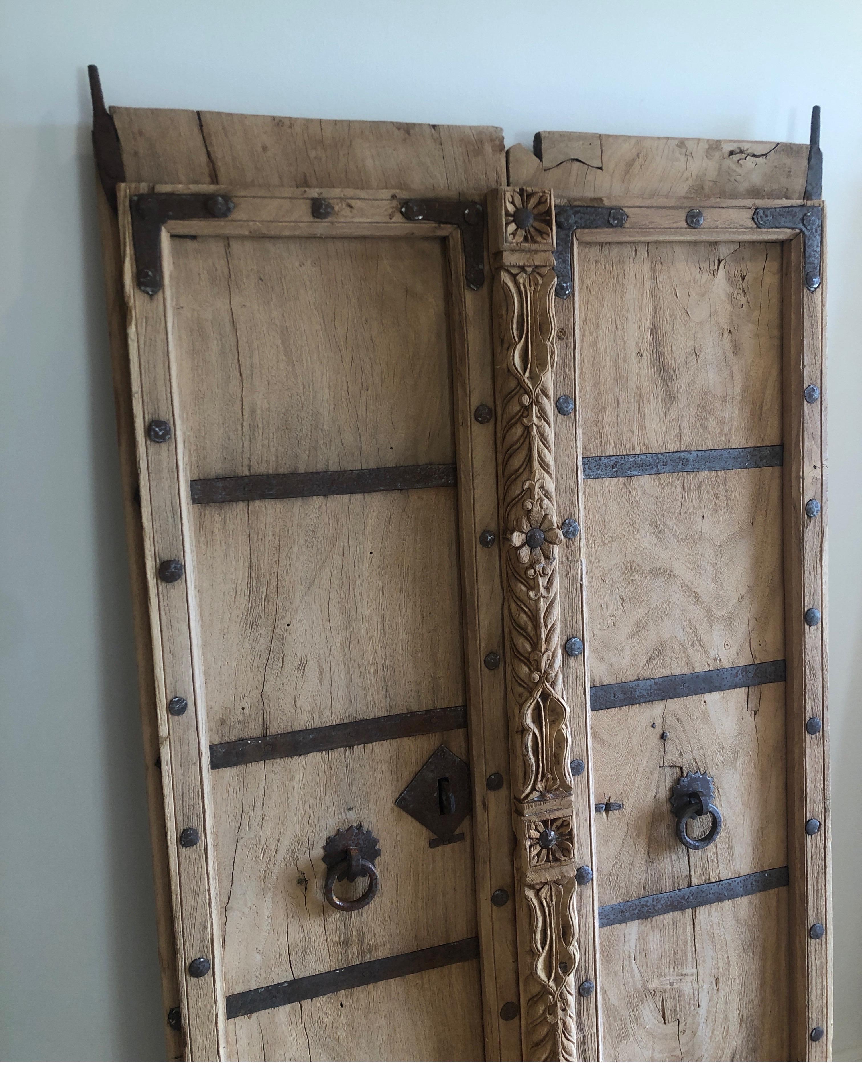 Individually hand crafted Teak door in early 20th century. Industrial metal details. 
Two salvaged doors that have been barred together to make one larger door/Gate. 

Does have scrapes, gauges, etc commensurate with age.

 