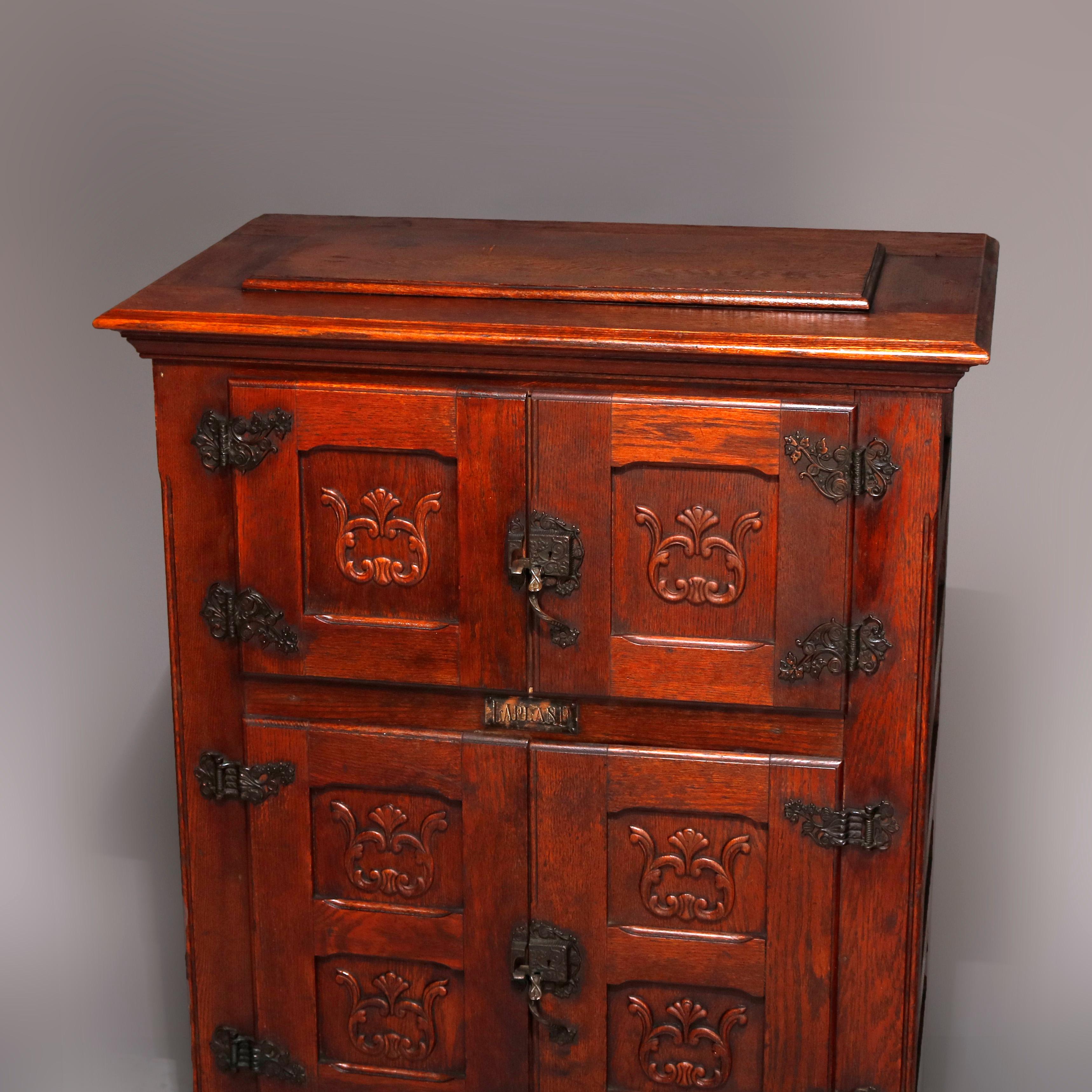 An antique Lapland ice box by Ranney Refrigerator Co. offers paneled oak construction with carved scroll and foliate reserves, caste foliate hardware, double door upper compartment over double door case with shelved interior, tin lined throughout,