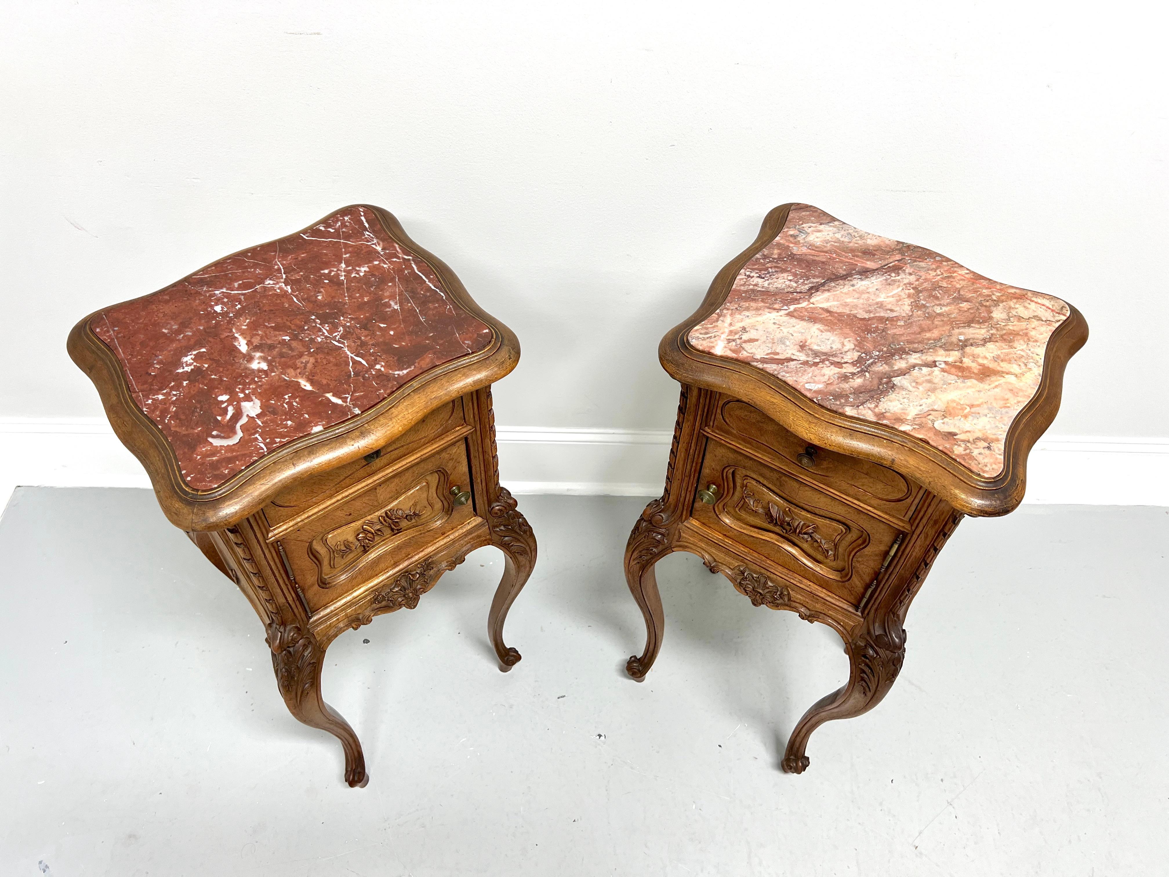 A pair of antique Early 20th Century French Country Louis XV style marble top commodes, unbranded. Chestnut with inset pink marble top, serpentine shape to bevel edge top, elaborately carved details, brass hardware, tall cabriole legs, and scroll