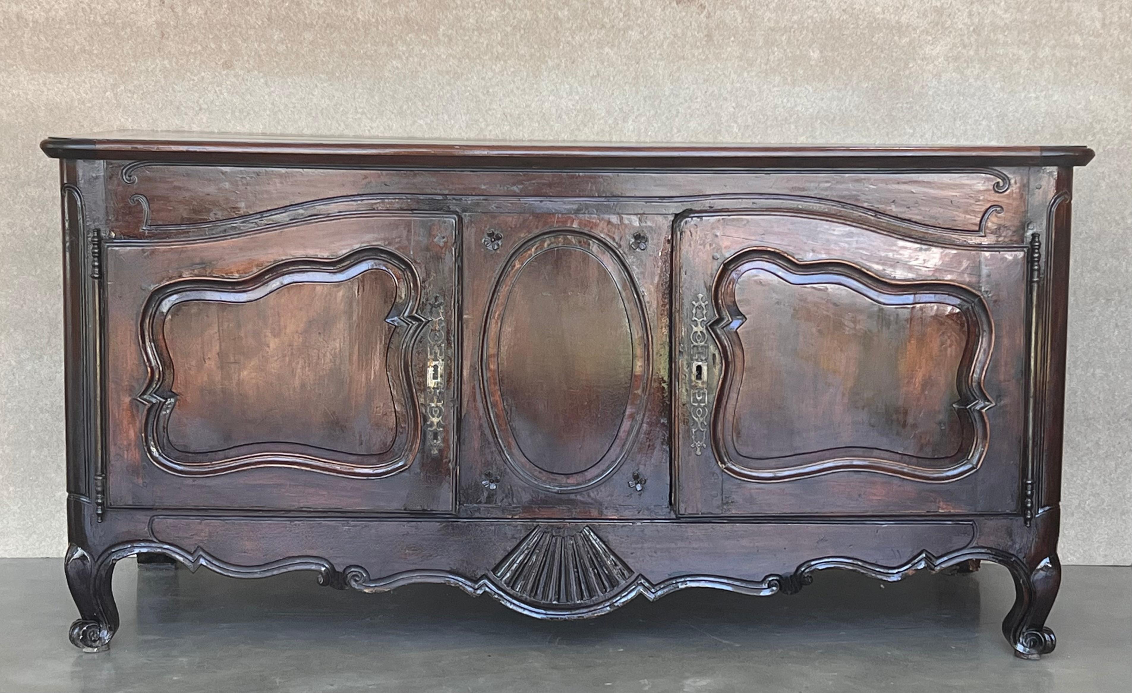 Ce grand buffet ancien en noyer de style Louis XIV est un chef-d'œuvre de l'art de l'ébéniste. Réalisé dans un somptueux noyer, il présente un design intrigant composé de deux armoires placées au-dessus d'un tablier magnifiquement sculpté qui est