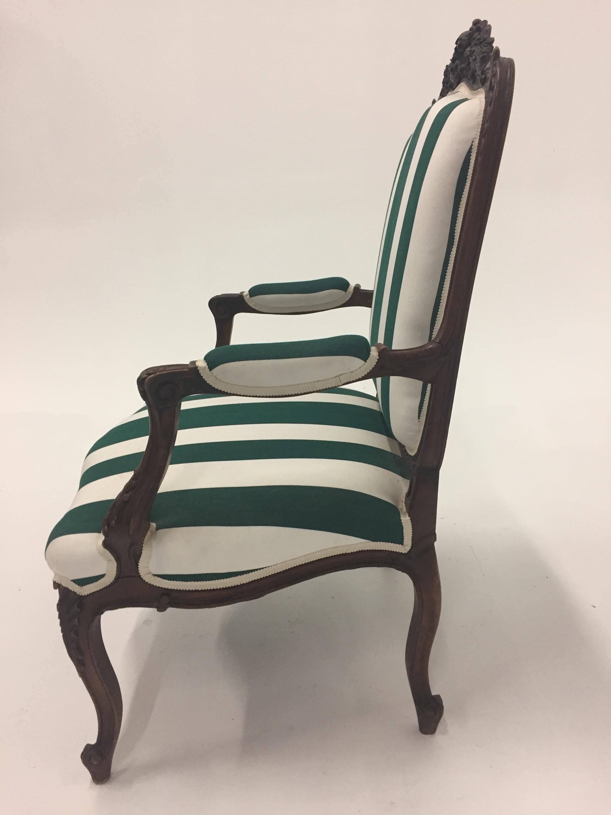 A large roomy carved walnut antique French bergere updated in green and white striped Sunbrella fabric, cleverly upholstered with vertical stripes on the front and horizontal stripes across the back.