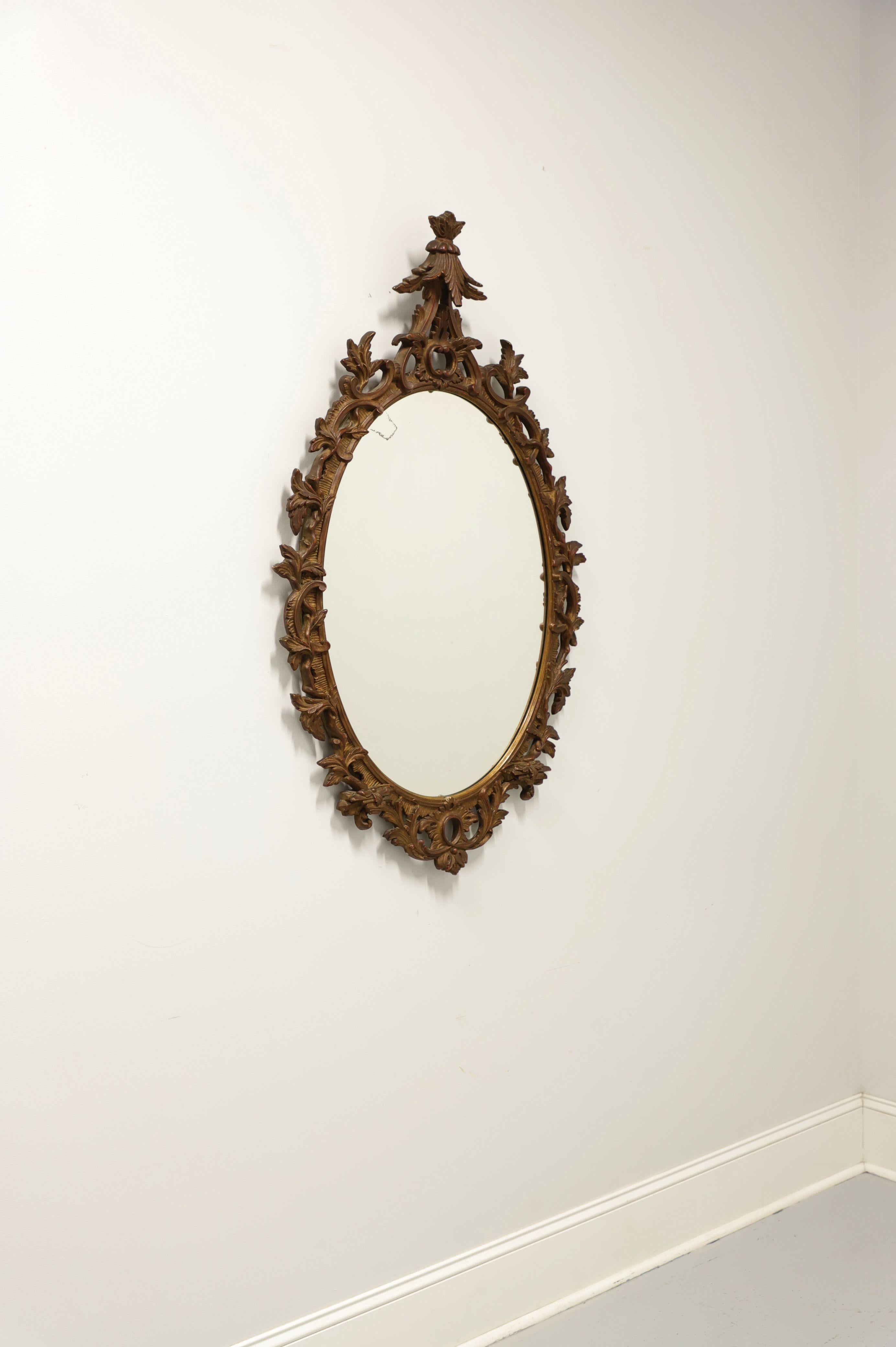 A Baroque style oval wall mirror by Charles of London. Mirrored glass with a carved wood frame painted bronze. Features ornate acanthus leaf carvings throughout and most decoratively to top. Likely made in England, in the early 20th