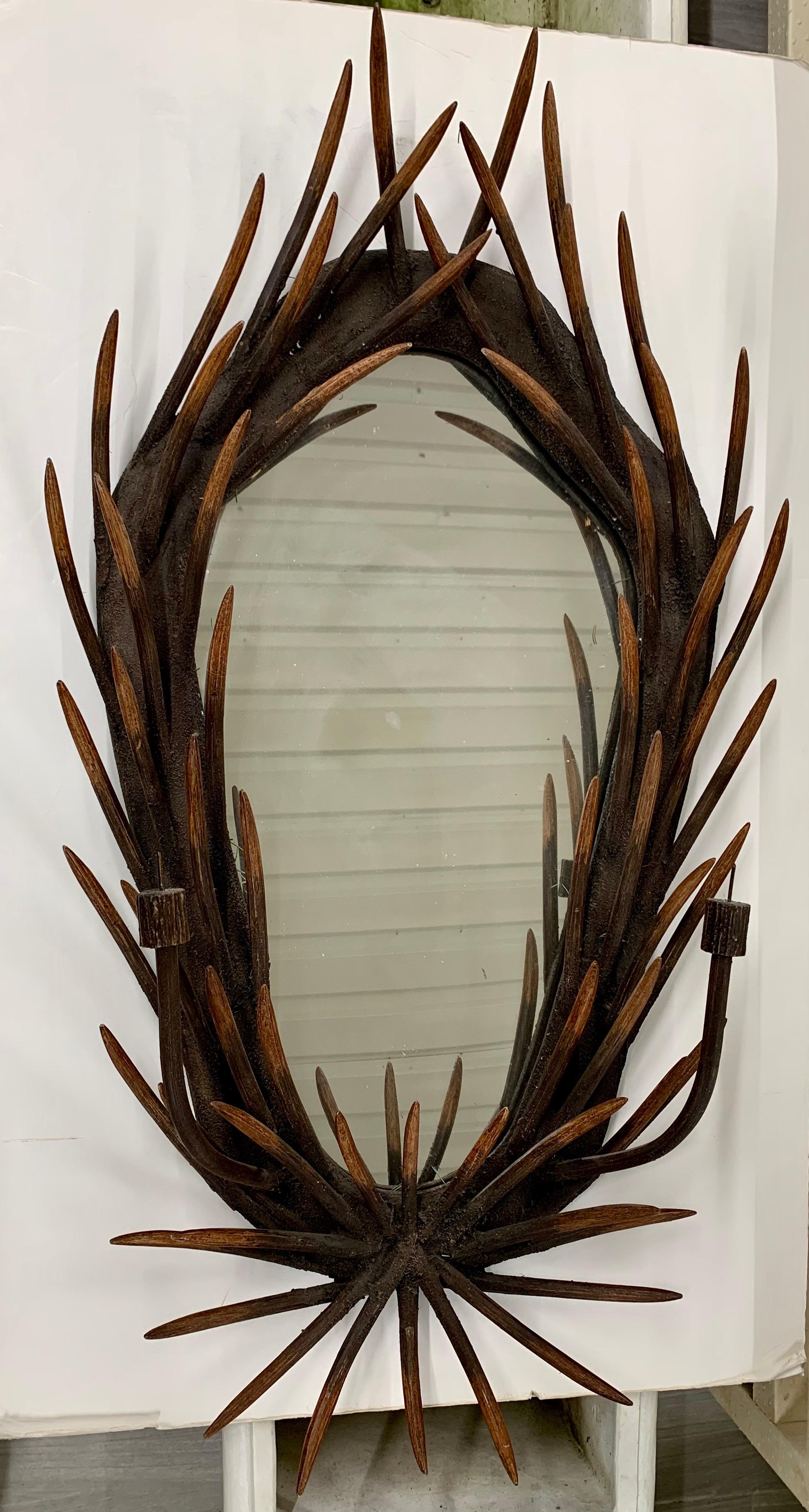 Unique oval wall mirror is comprised of carved wood made to look like deer antlers surrounding an oval mirror. Each side has an iron candleholder.