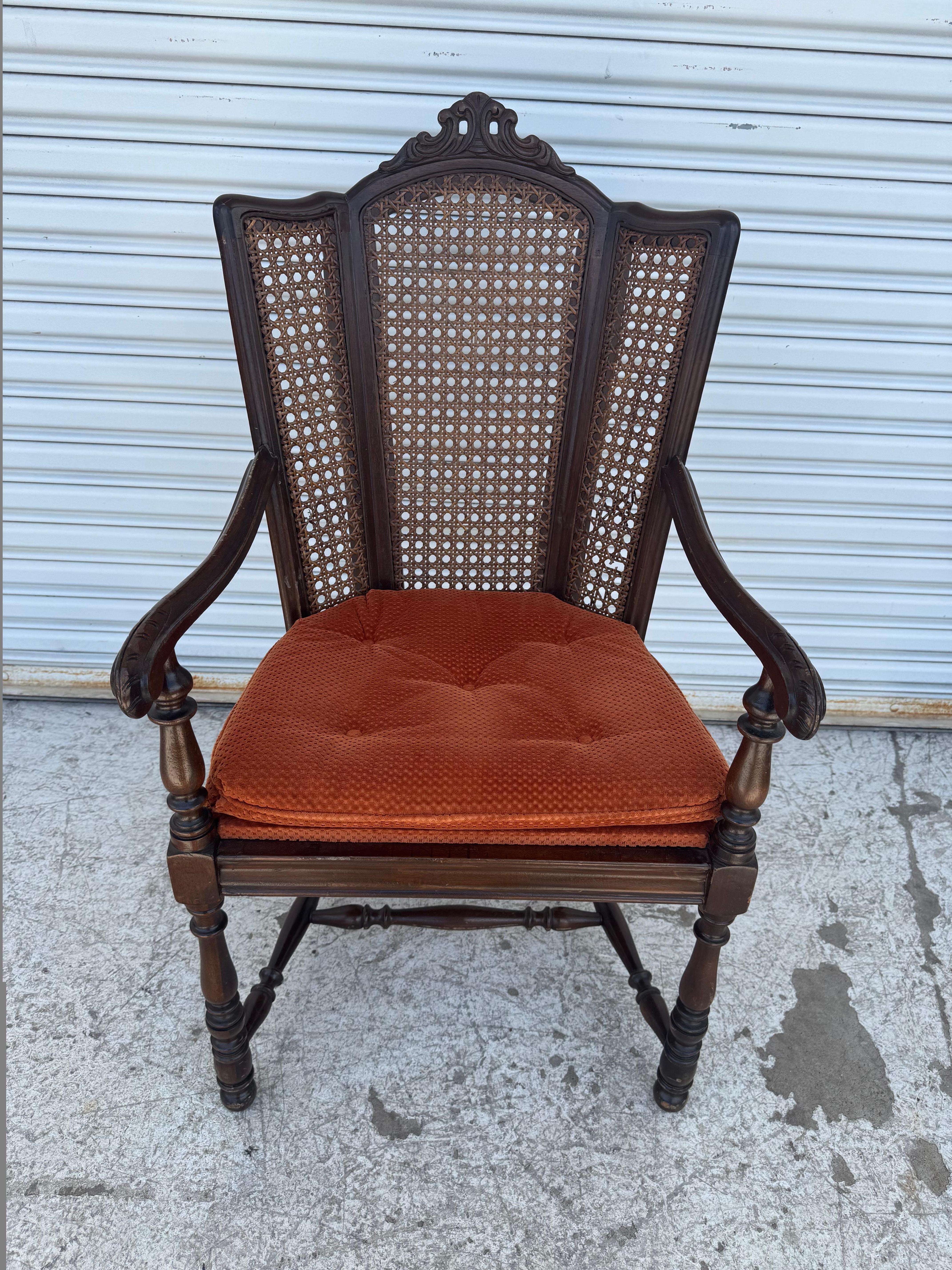 This stunning antique armchair features an intricately carved wooden frame with a unique cane backrest design that brings an airy elegance to its stately presence. The rich dark wood showcases fine craftsmanship, while the ornately carved crest adds