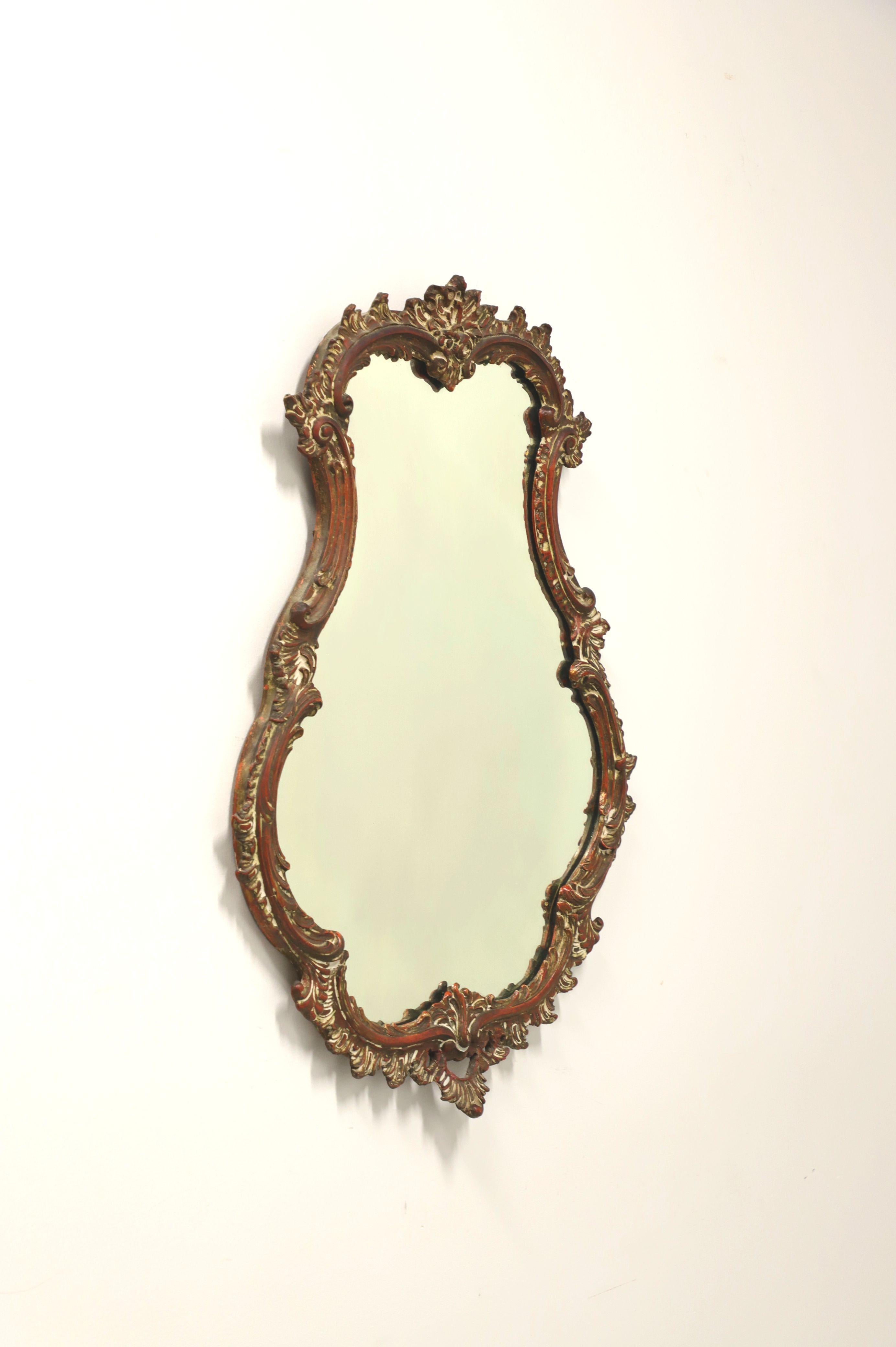 An antique French style wall mirror, unbranded. Mirrored glass and wood frame painted gold, with shades of red & white. Features an ornately carved frame with a decorative motif. Possibly made in USA, in the late 19th Century. 

Measures: 26.5 W