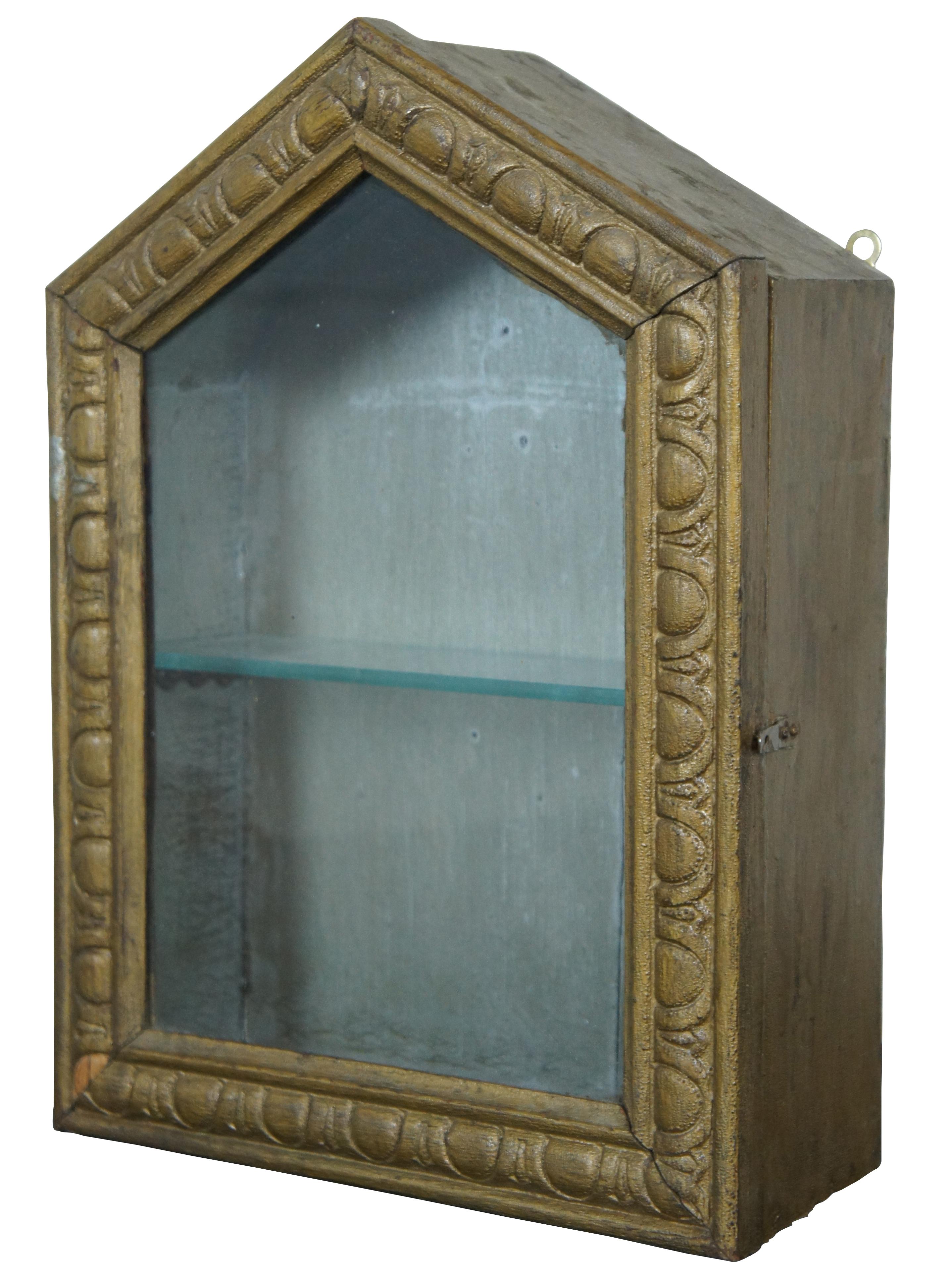 Antique gold painted wood & glass front wall hanging curio or bathroom cabinet with a peaked front and carved details, white painted interior, and one glass shelf inside.
 