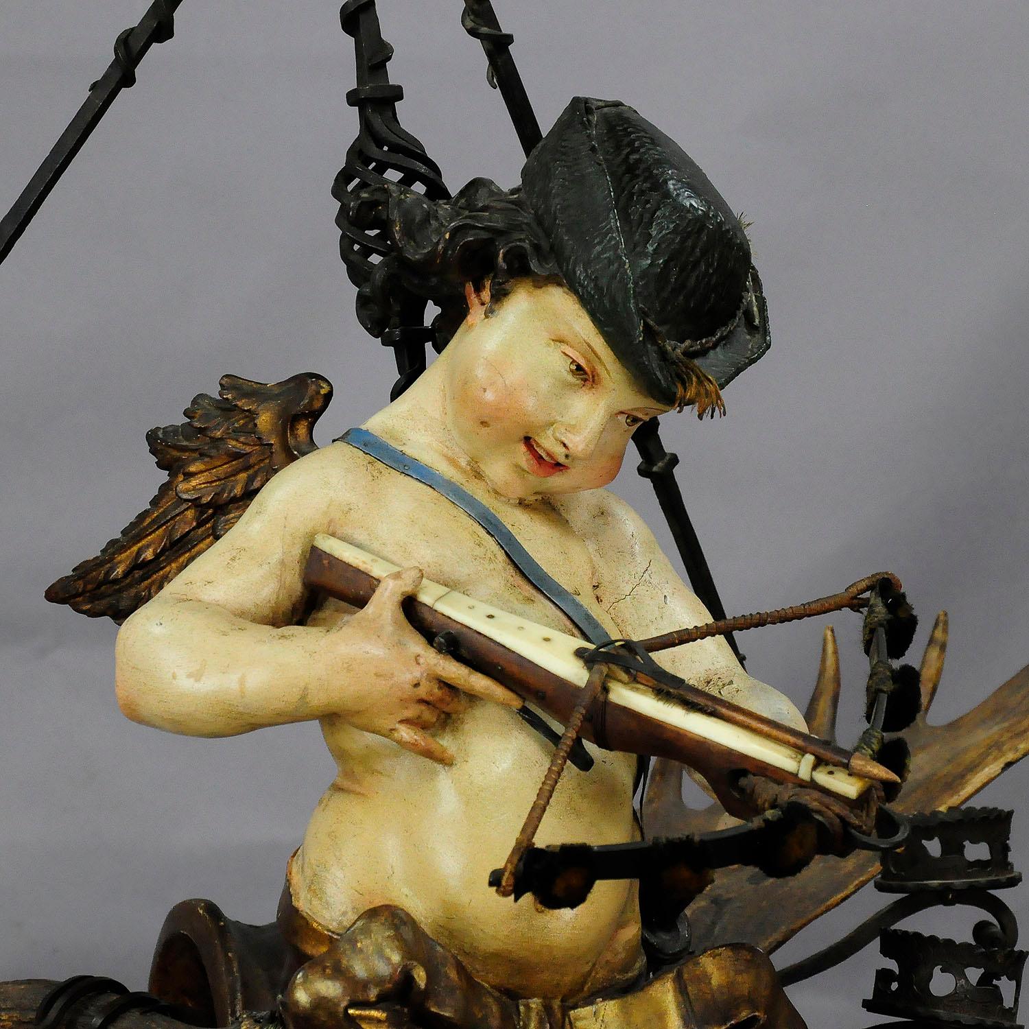An unique and rare antique antler chandelier - a wooden hand carved and painted statue of an angel of love as hunter with crossbow fixed on an impressive pair of original fallow deer antlers executed circa 1880. Executed with several splendid
