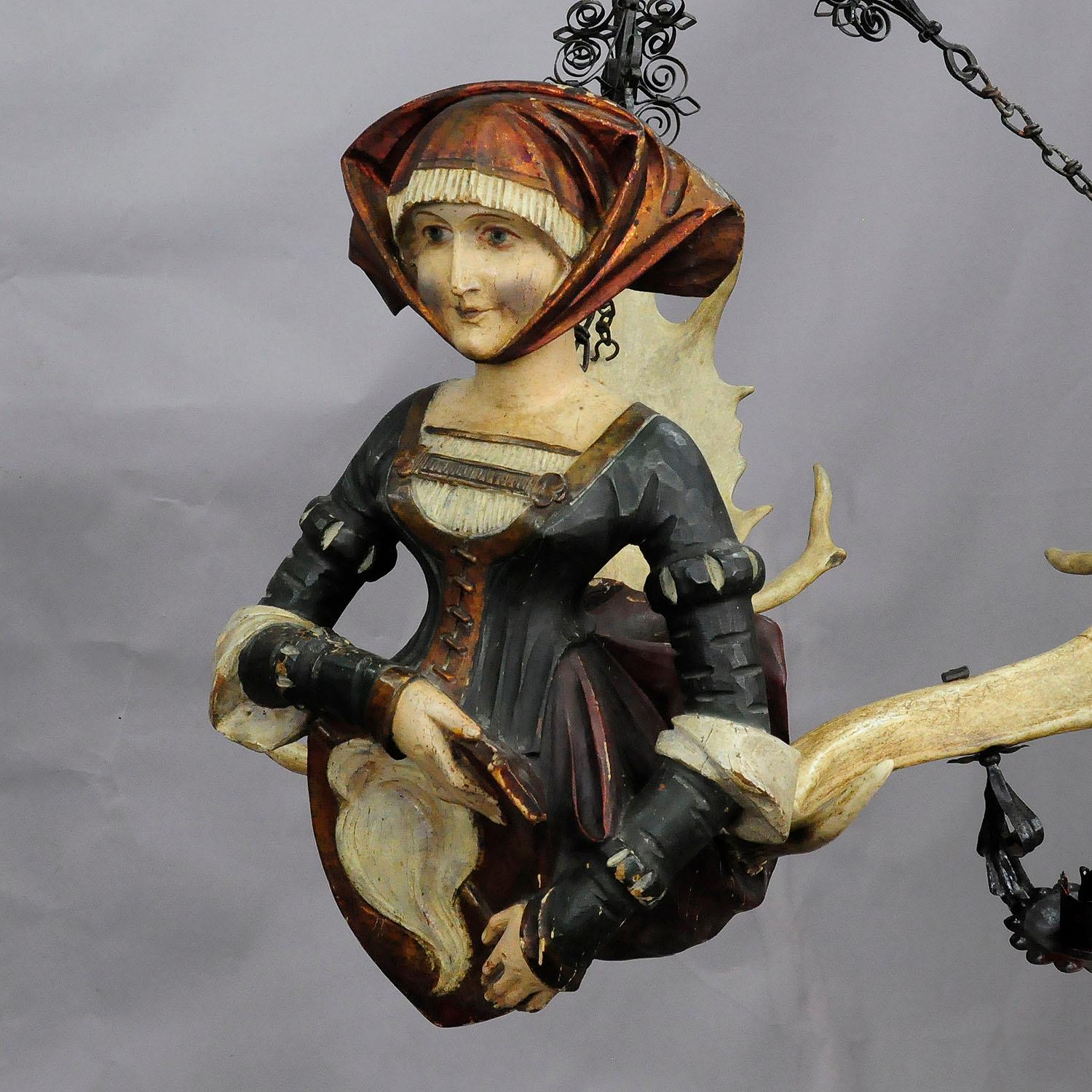 An antique antler chandelier, a wooden hand carved and painted statue of a victorian lady fixed on a large pair of original fallow deer antlers. Named lusterweibchen or lüsterweibchen, executed circa 1900. with hand forged iron suspension and 4 hand