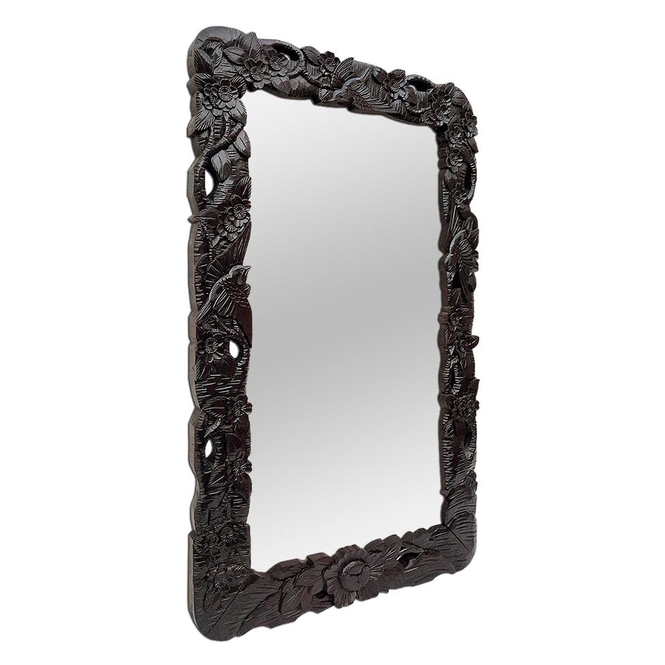 Antique wall mirror in blackened exotic wood, finely carved in a composition with floral and birds decoration. Antique French mirror, Indonesian style inspiration, circa 1920. Modern glass mirror. Antique frame width 9 cm / 3.54 in. Antique wood
