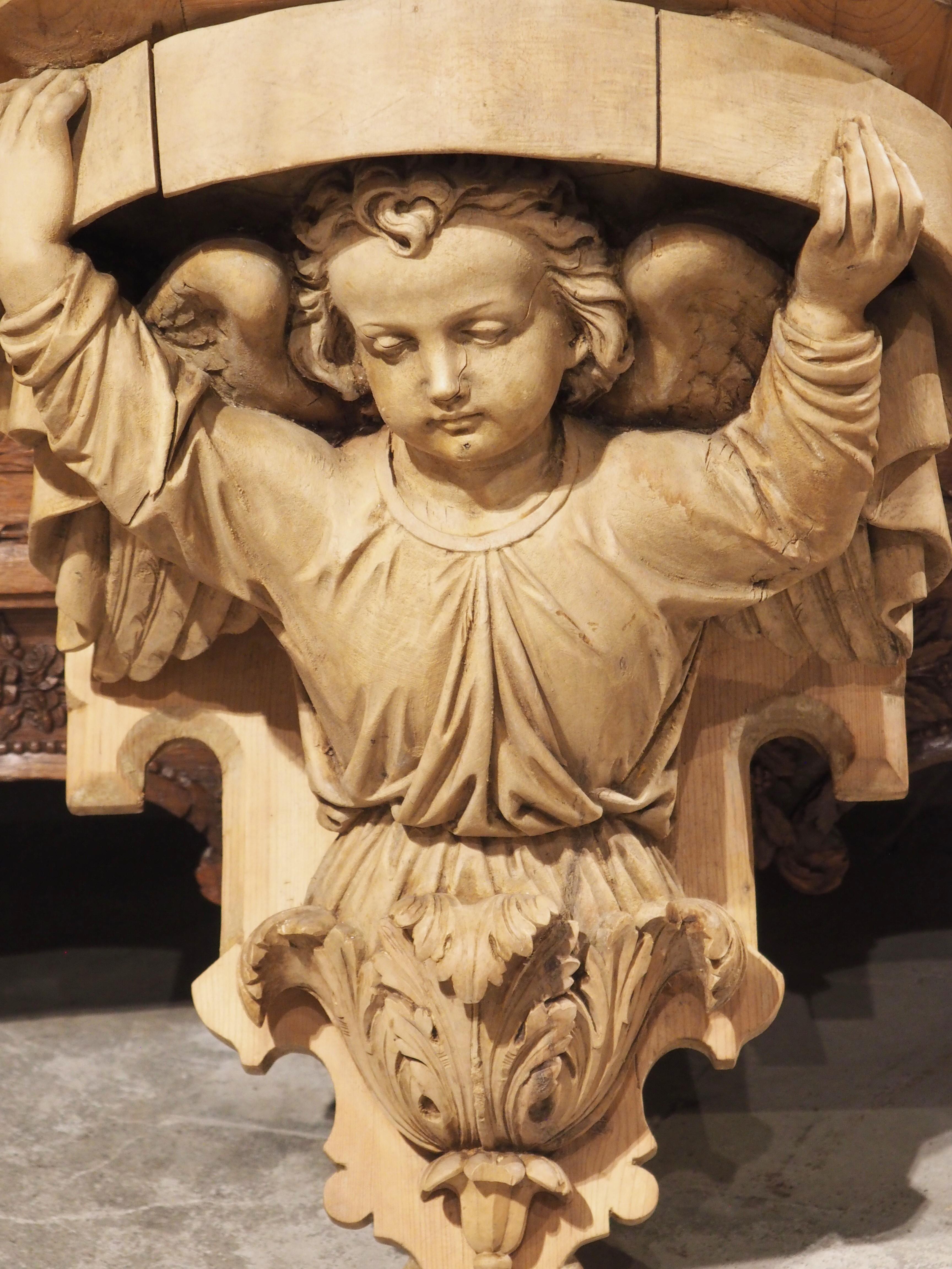 Hand-carved in France, circa 1880, this wooden bracket console features a wonderfully executed winged angel beneath an angular entablature. The innocent visage of the cherub is augmented by the downward gaze, as he supports an arched molding above