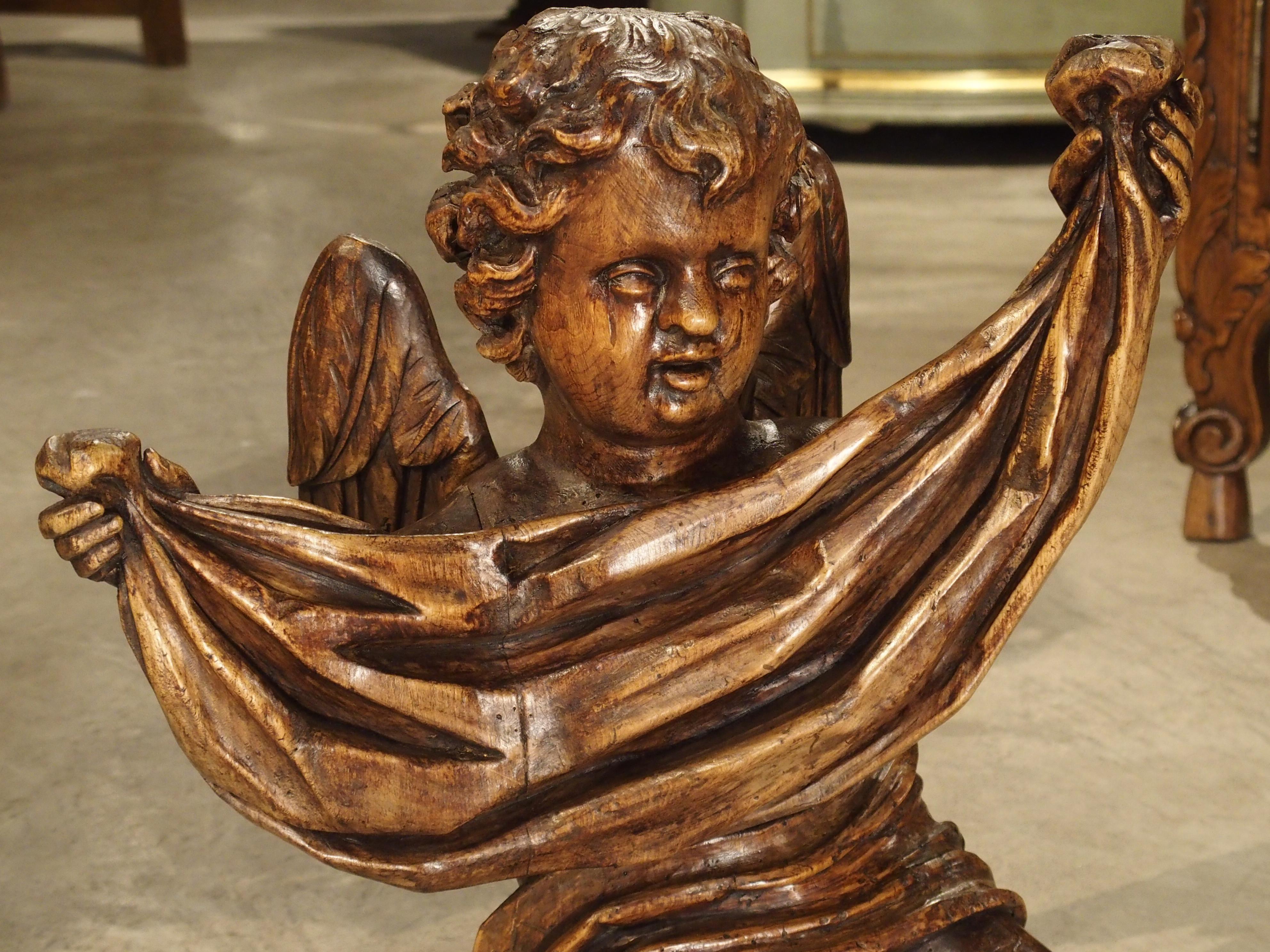 This hand carved seated cherub is of a nice size at nearly 23 inches tall. The cherub is holding a piece of draped cloth in front of its chest and still has both wings intact. The sculptor who carved this cherub was very good at the figural