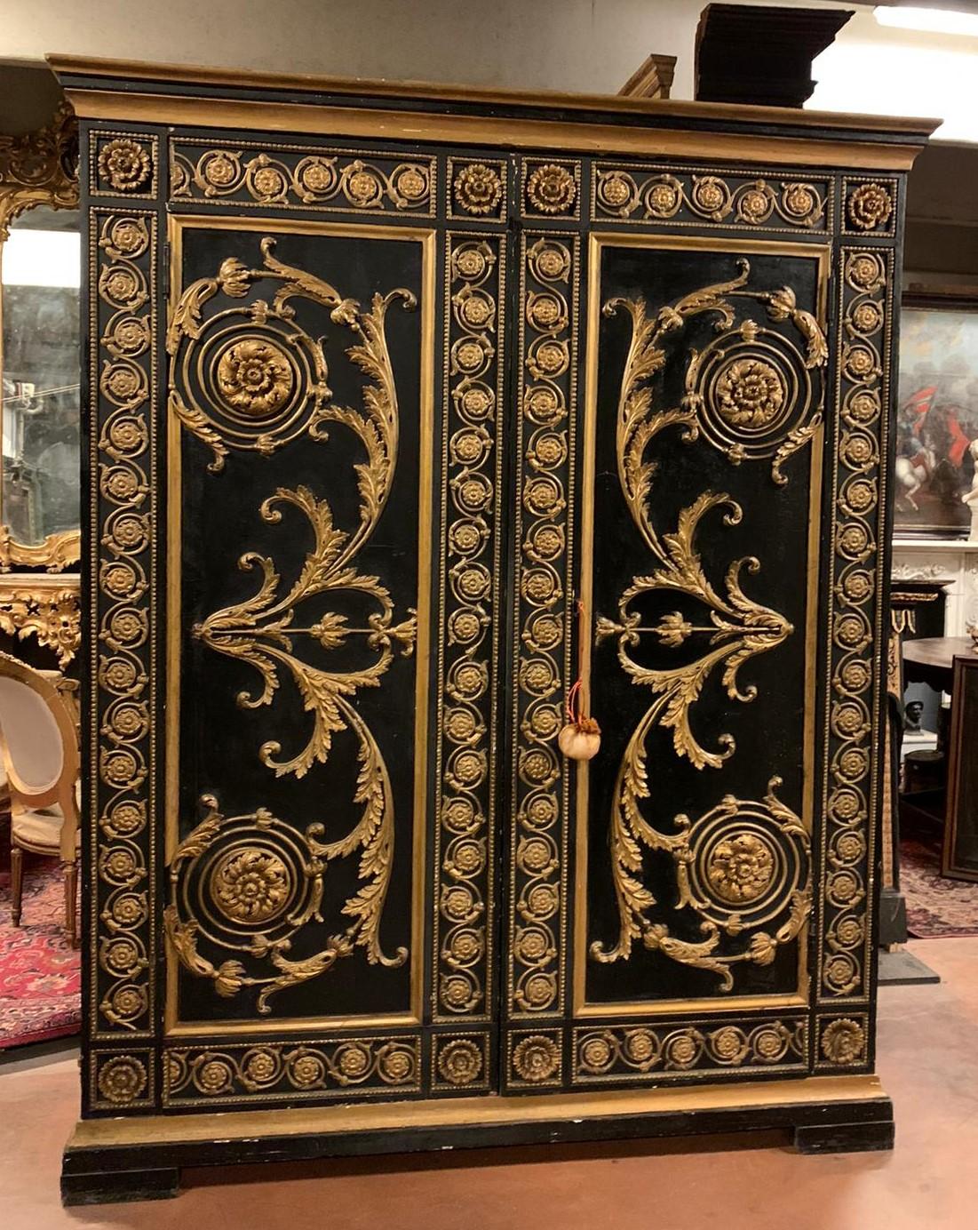 Antique wardrobe or large cabinet in richly carved wood, hand-lacquered on a black background and gilded in the sculptures, built entirely by hand in the 19th century in Italy.
It has a back in less noble and posthumous wood, but still retains the