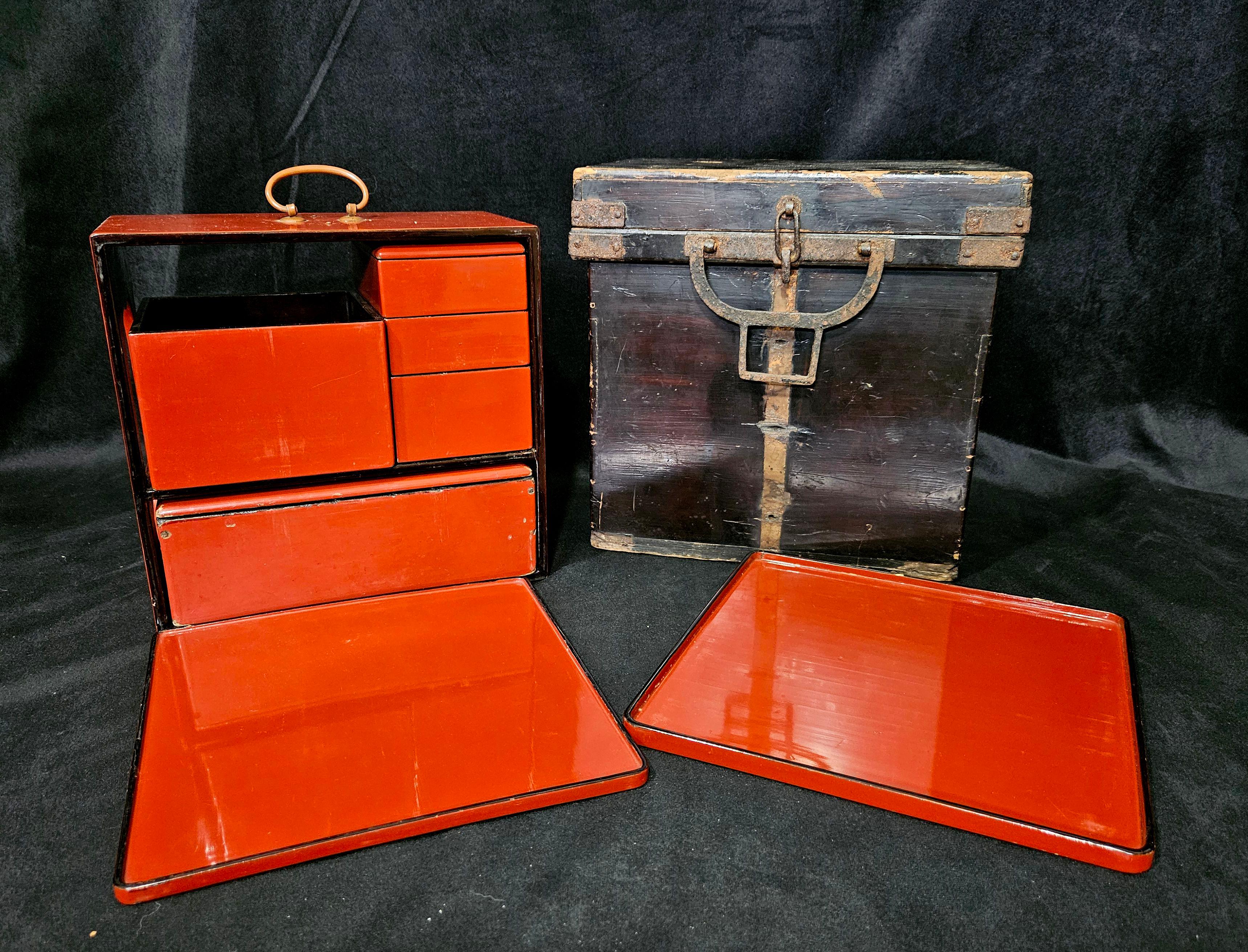 Meiji Period Red and Black Lacquer Food Carrier Set, with top handle, drawers with two bowls and a serving spoon, plus three stacked boxes, and two square trays, contained within an iron-bound black painted wooden carry case, OS: 9 3/4