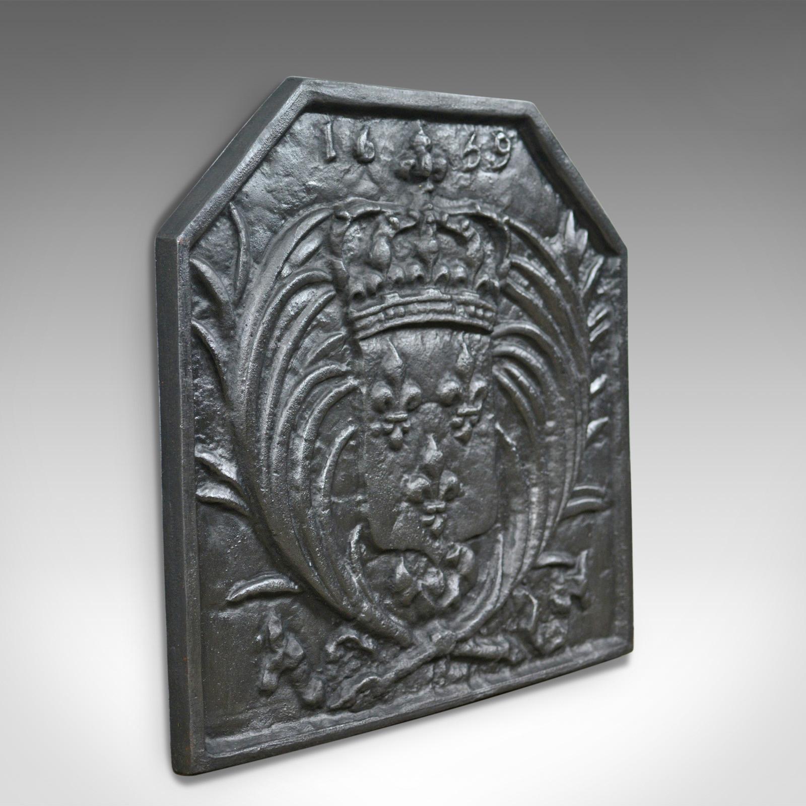 This is an antique cast iron fire back displaying a coat of arms. A heavy fire plate to back a fireplace and retain heat. A revival casting crafted in the early 20th century.

Heavy fire back in cast iron with a graphite finish
Featuring a canted