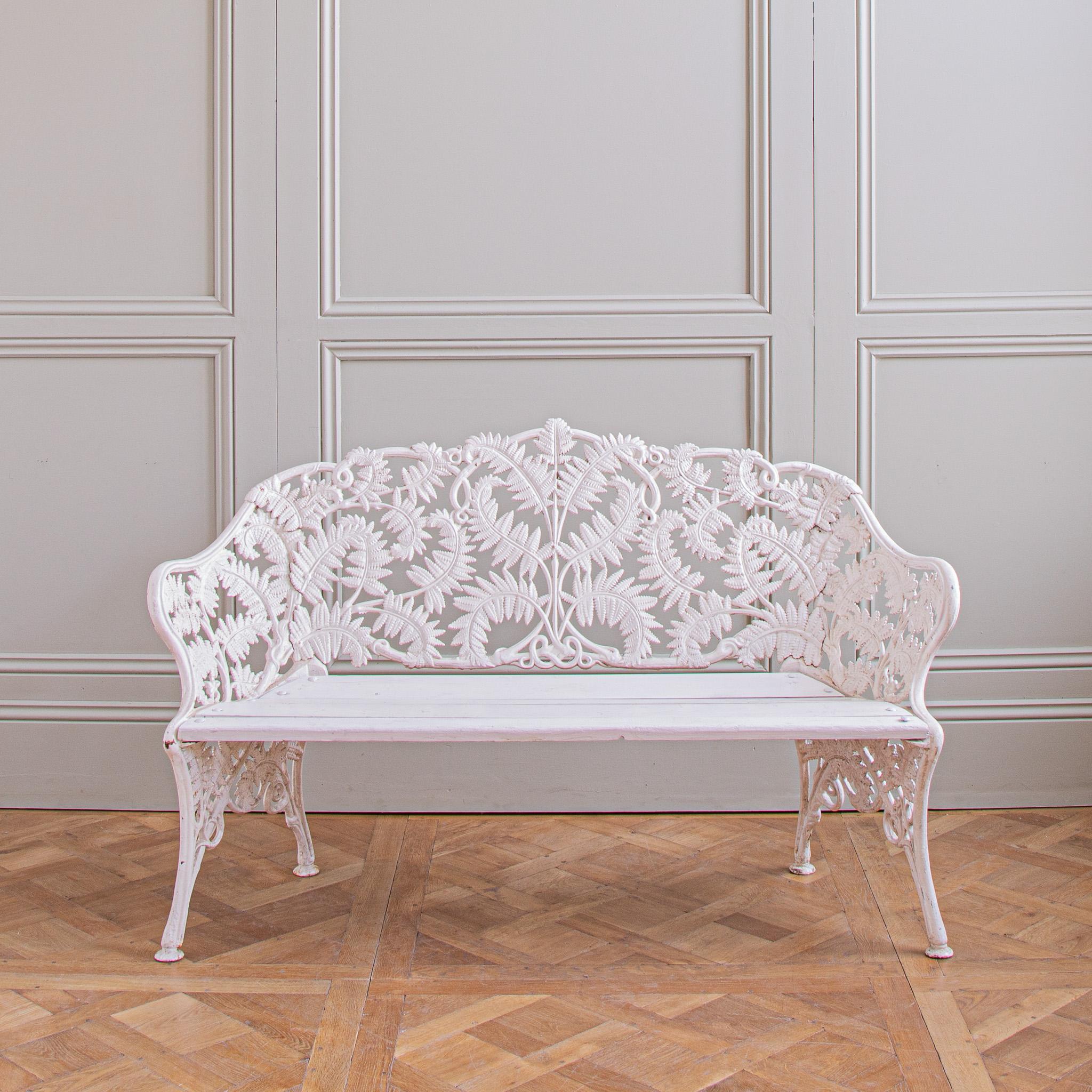 An antique, cast iron garden bench, circa 1920. The fern motifs on this particular design, bought in the South of France, are more animated and lively than others of this type. The bench is a generous 2 seater and painted white.