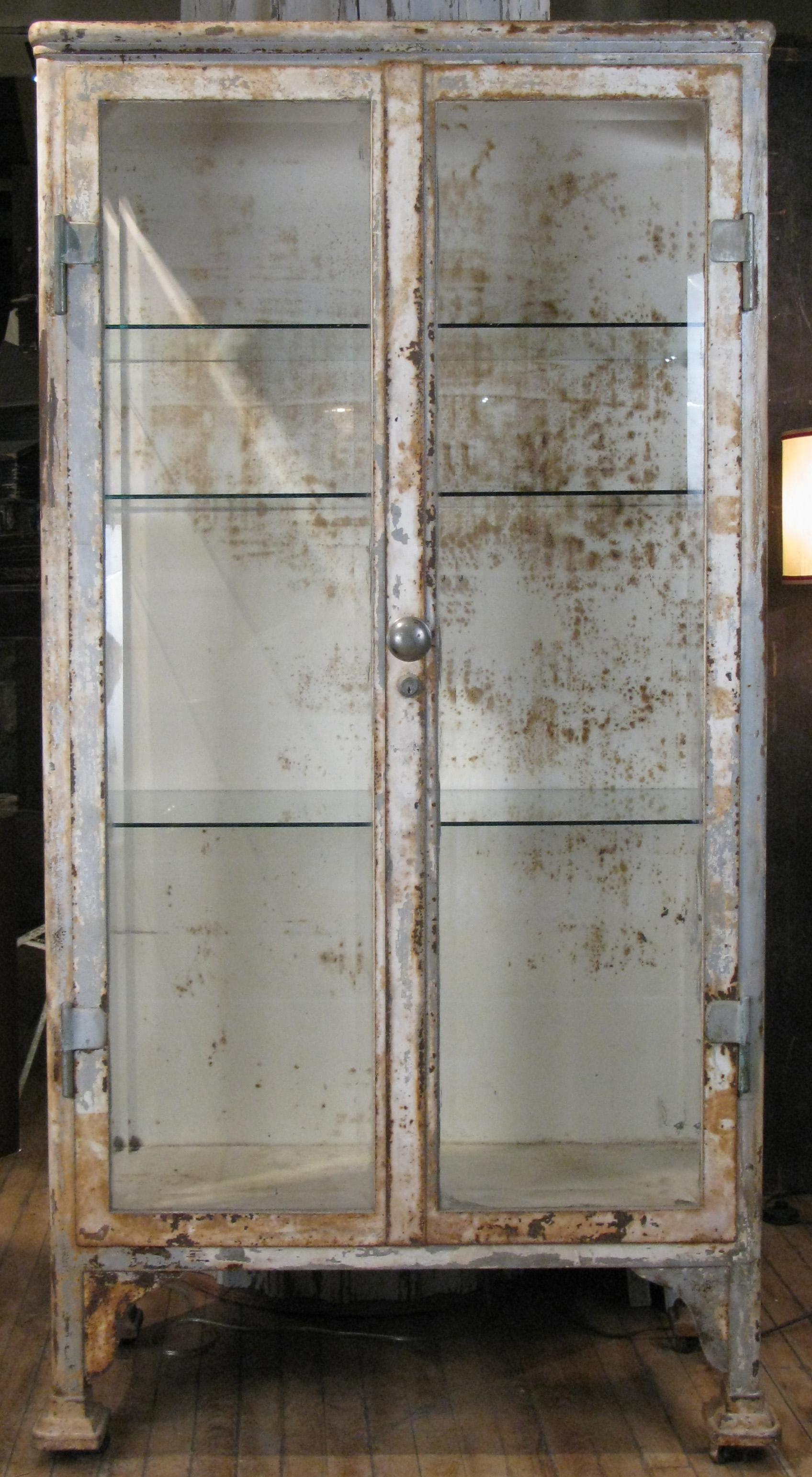 A very handsome antique 1930s apothecary or display cabinet with a cast iron and steel frame, and beveled glass doors and side panels. With glass shelves. In its original distressed white finish. One of the most substantial apothecary cabinets from