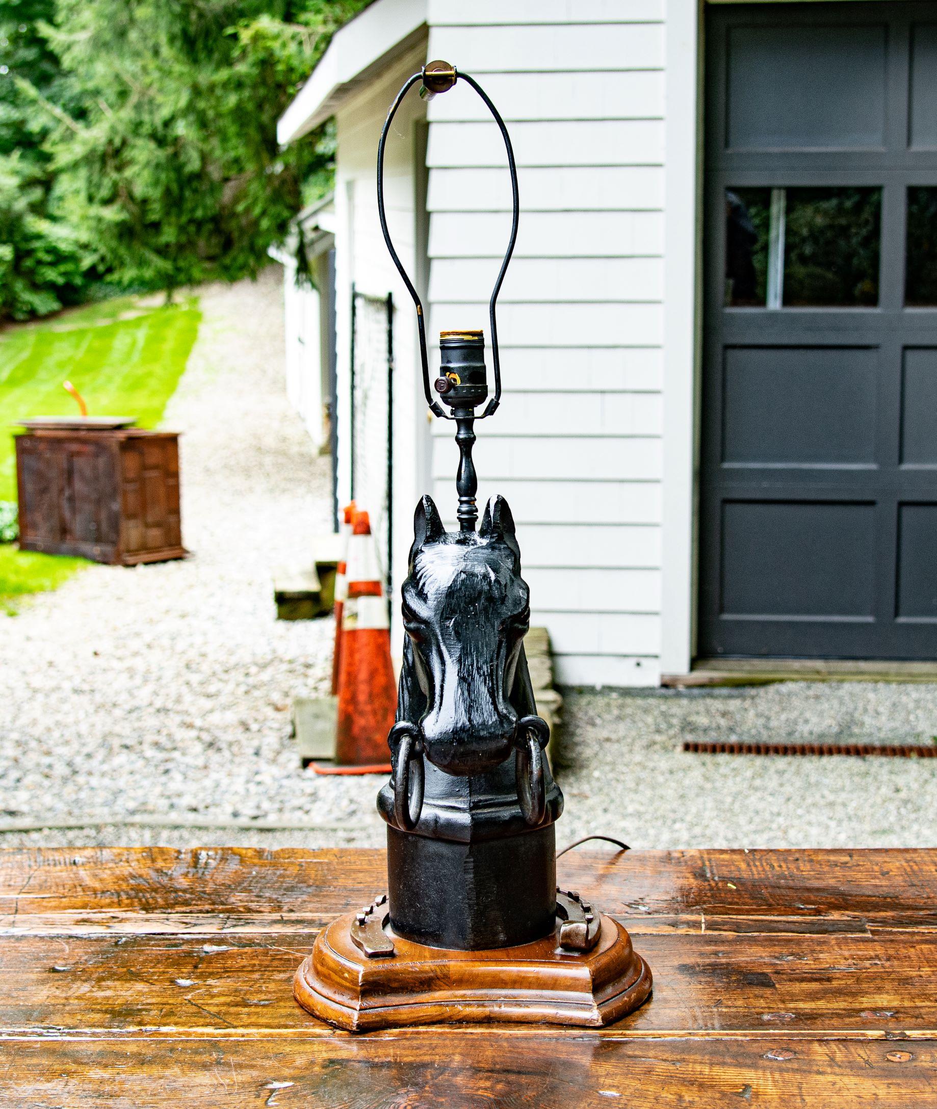 Black-painted cast iron horse head hitching post finial lamp, American, late 19th-early 20th century, the large antique with double rings atop columnar pedestal, sitting on a base made of oak surrounded by a brass horseshoe.
