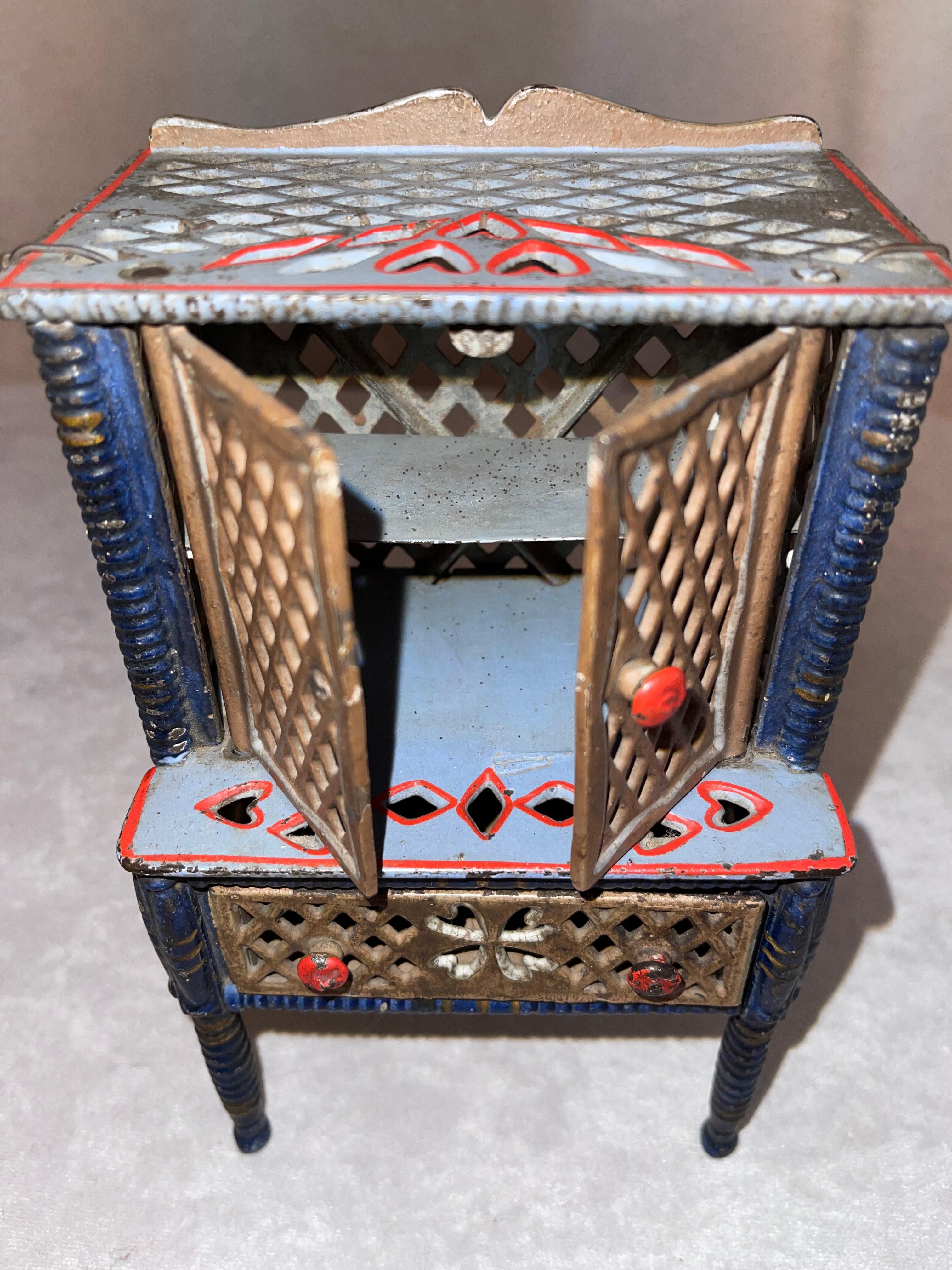This cast iron cabinet has all the little extras that make it fun. The doors on top open to reveal an original shelf. There is a working drawer, and above all the paint is original and in very good condition.
 If you like miniatures, here is a nice