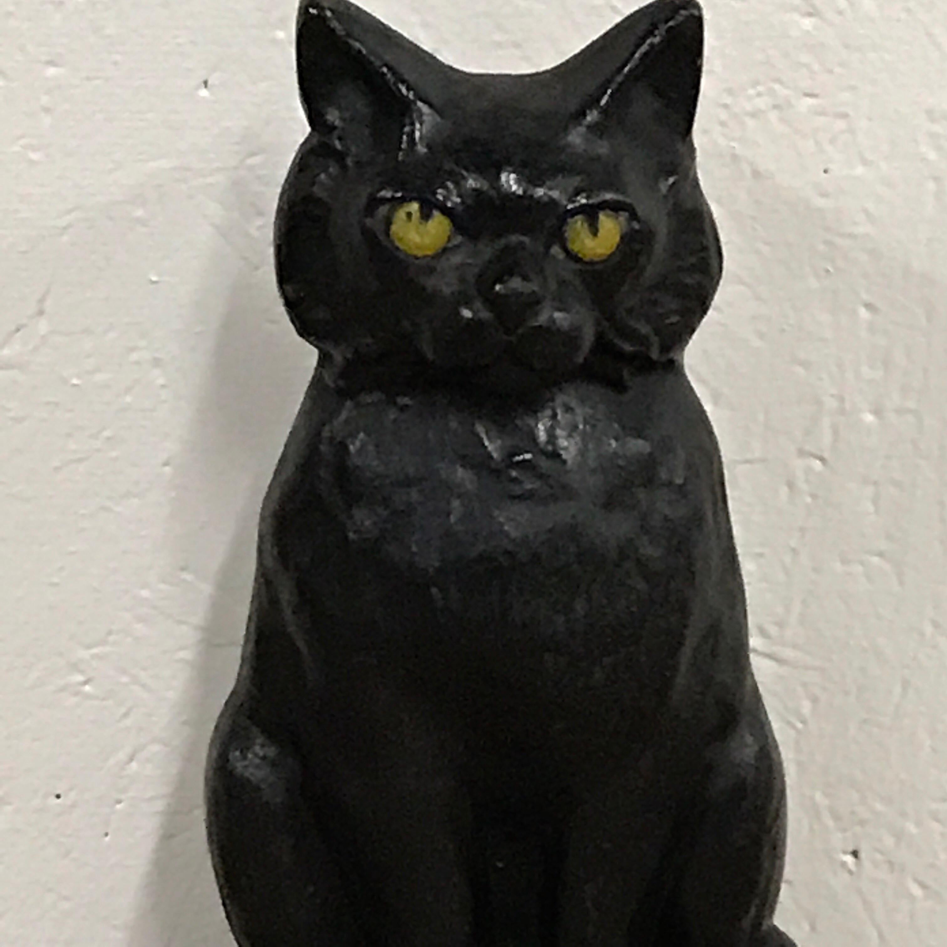 Antique cast iron seated cat doorstop seated on a stoop with an expressive face.