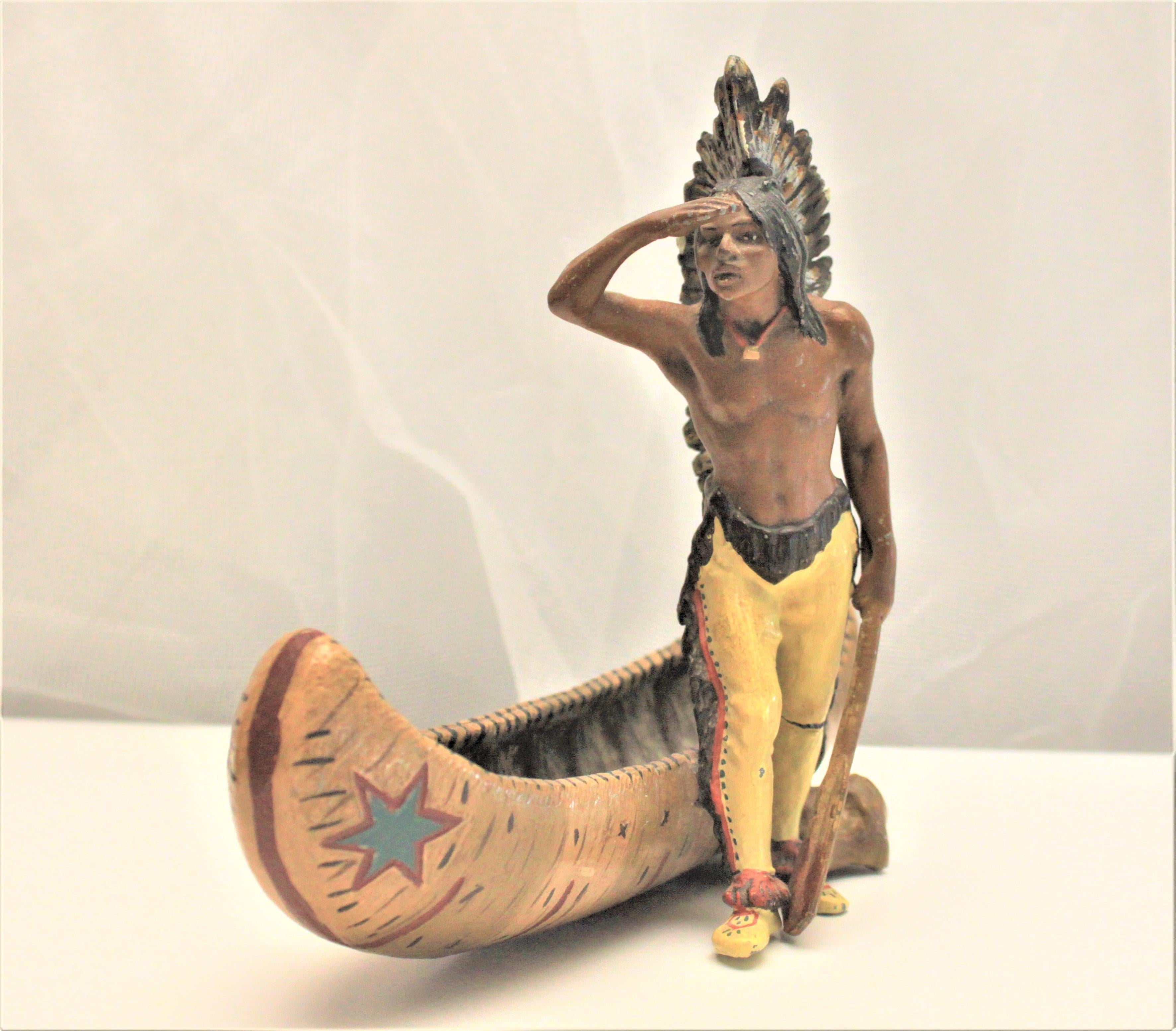 This ornately cast and cold painted figurine is presumed to be composed of spelter and depicts a Native American warrior standing beside a canoe. The figurine is unmarked, so no maker can be determined definitively, but is believed to have been made