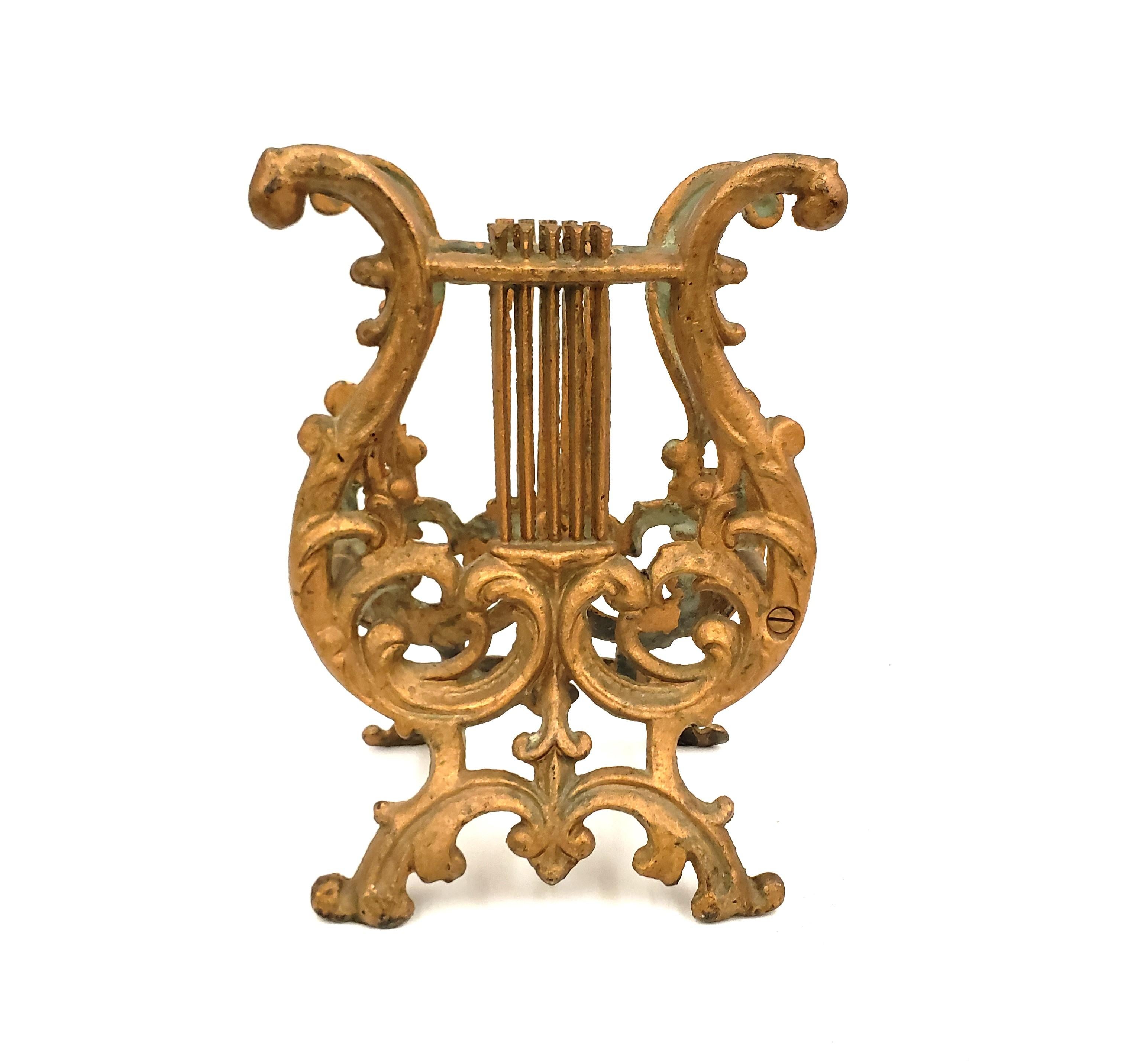This antique book stand is unsigned, but presumed to have originated from the United States and date to approximately 1920 and done in the period style. The stand is composed of a cast metal lyre on both ends with a sturdy base and gilt finish.