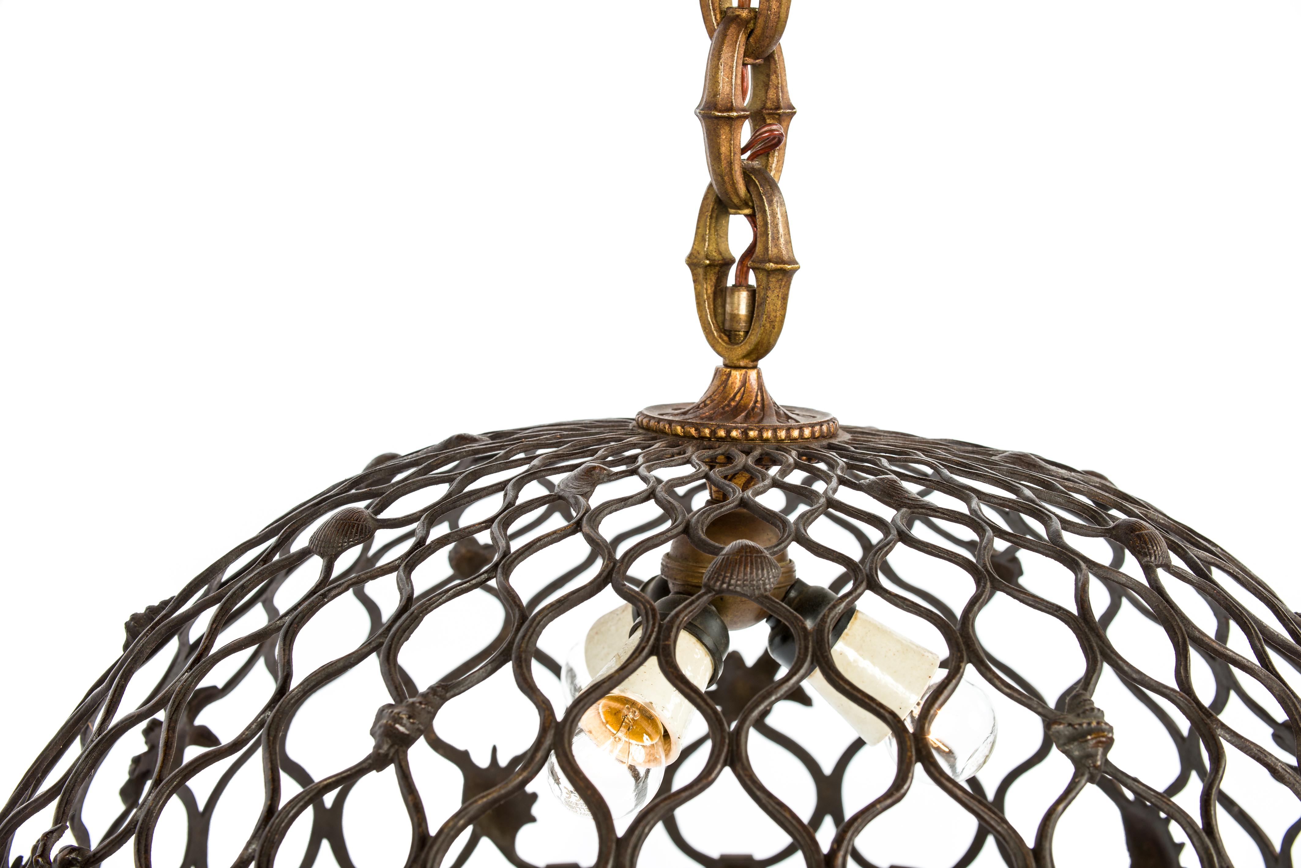 This beautiful pendant was made in France in the early 20th century, circa 1920. It was cast in bronze and is equipped with three E27 light fixtures. The lamp is designed to resemble a stylized fishing net that is decorated with various shells and