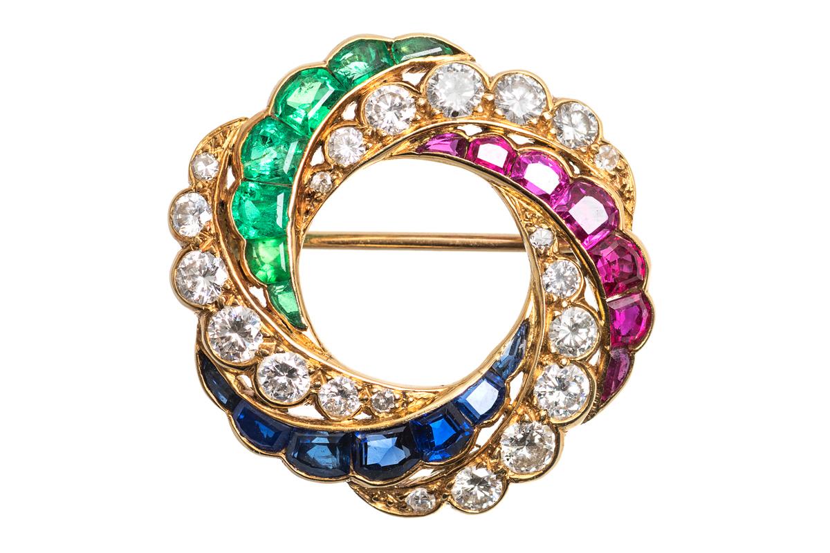 Antique brooch in the form of a stone set catherine wheel mounted in 18 carat yellow gold. The design comprises alternate crescents of brilliant cut diamonds, shaped Burma rubies, Ceylon sapphires, and Columbian emeralds.
Measures 27mm