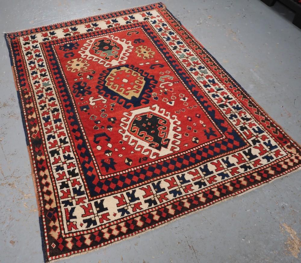 Ancien tapis caucasien Bordjalou Kazak au dessin très abstrait. Ce sont les tapis Kazak les plus septentrionaux.
Circa 1870

Le tapis présente trois grands médaillons à crochets sur un champ rouge garance, avec de nombreux éléments de remplissage
